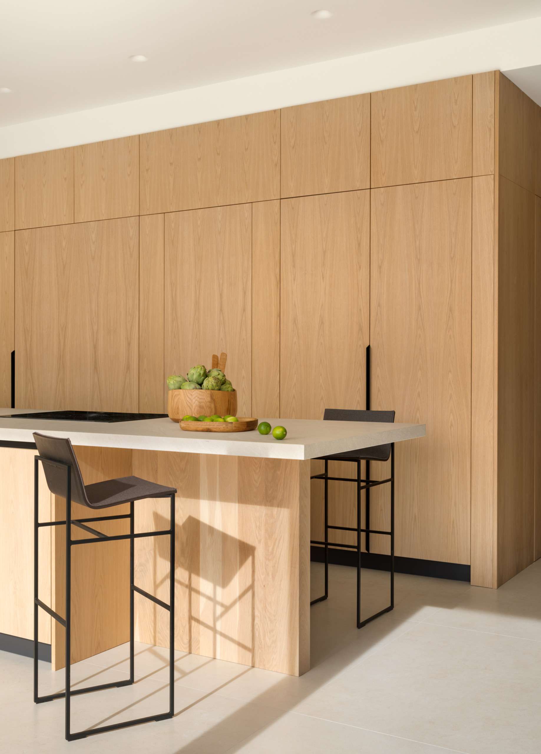 This light-filled kitchen embraces simplicity with flat-front oak cabinetry and a sleek stone topped island. Floor-to-ceiling doors blur the line between indoors and out, creating an airy transition to the natural landscape beyond.