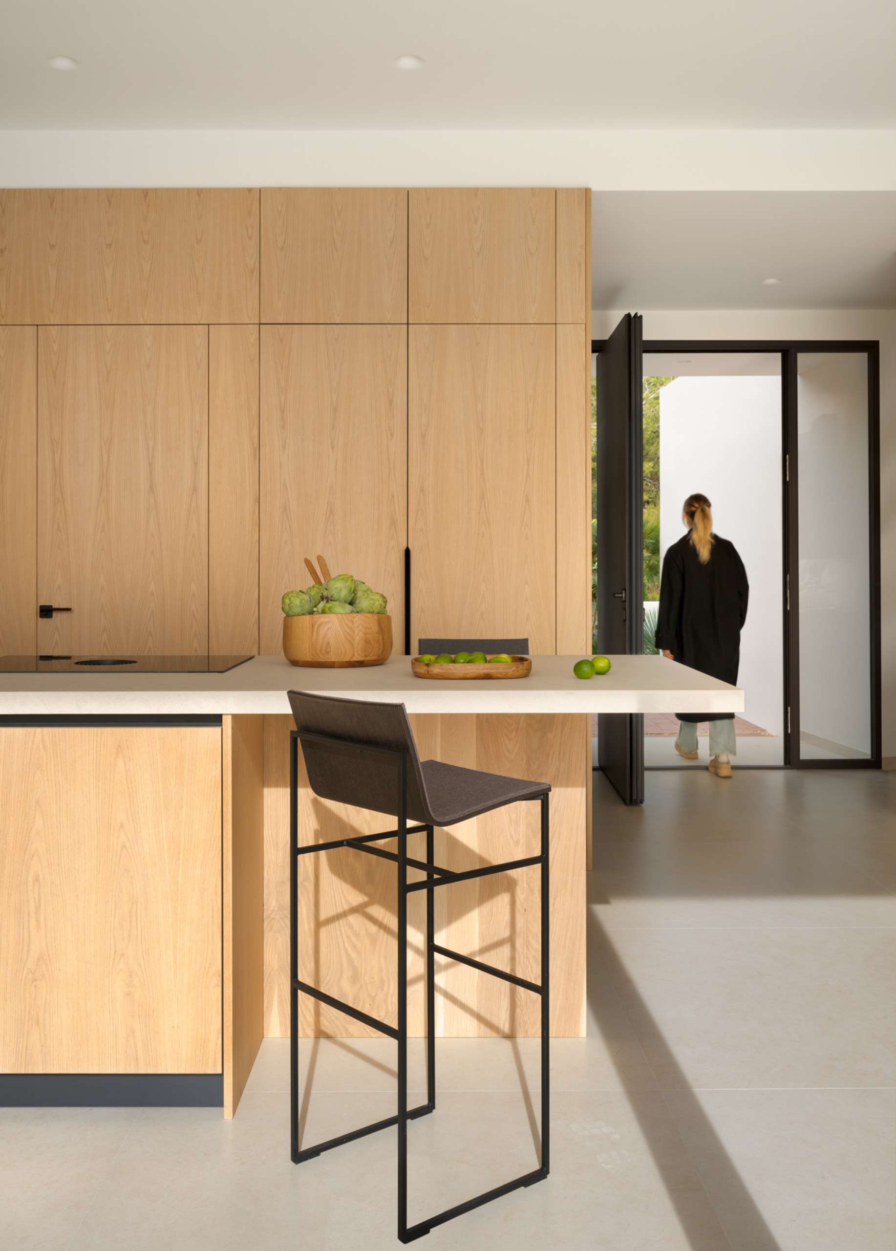 This light-filled kitchen embraces simplicity with flat-front oak cabinetry and a sleek stone topped island. Floor-to-ceiling doors blur the line between indoors and out, creating an airy transition to the natural landscape beyond.