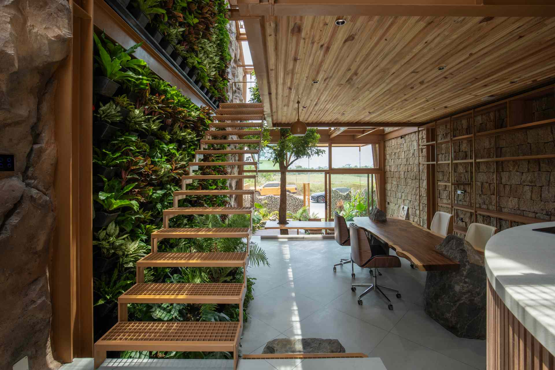 Steel stairs with an open-grid design bring an industrial edge while keeping things light and airy. One side frames a lush vertical garden, the other opens to natural stone and glass, blending raw materials with greenery and light.