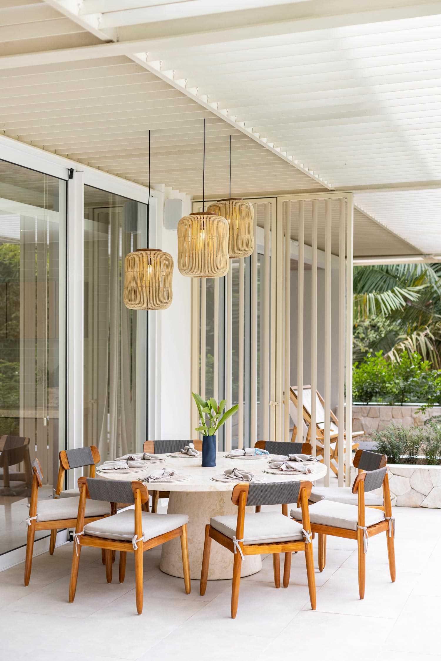 Nestled beneath a canopy of greenery, this intimate outdoor dining area features a round table surrounded by stylish wood chairs, creating the perfect blend of rustic warmth and modern comfort. Ambient lighting and nearby lush plants add to the inviting atmosphere.