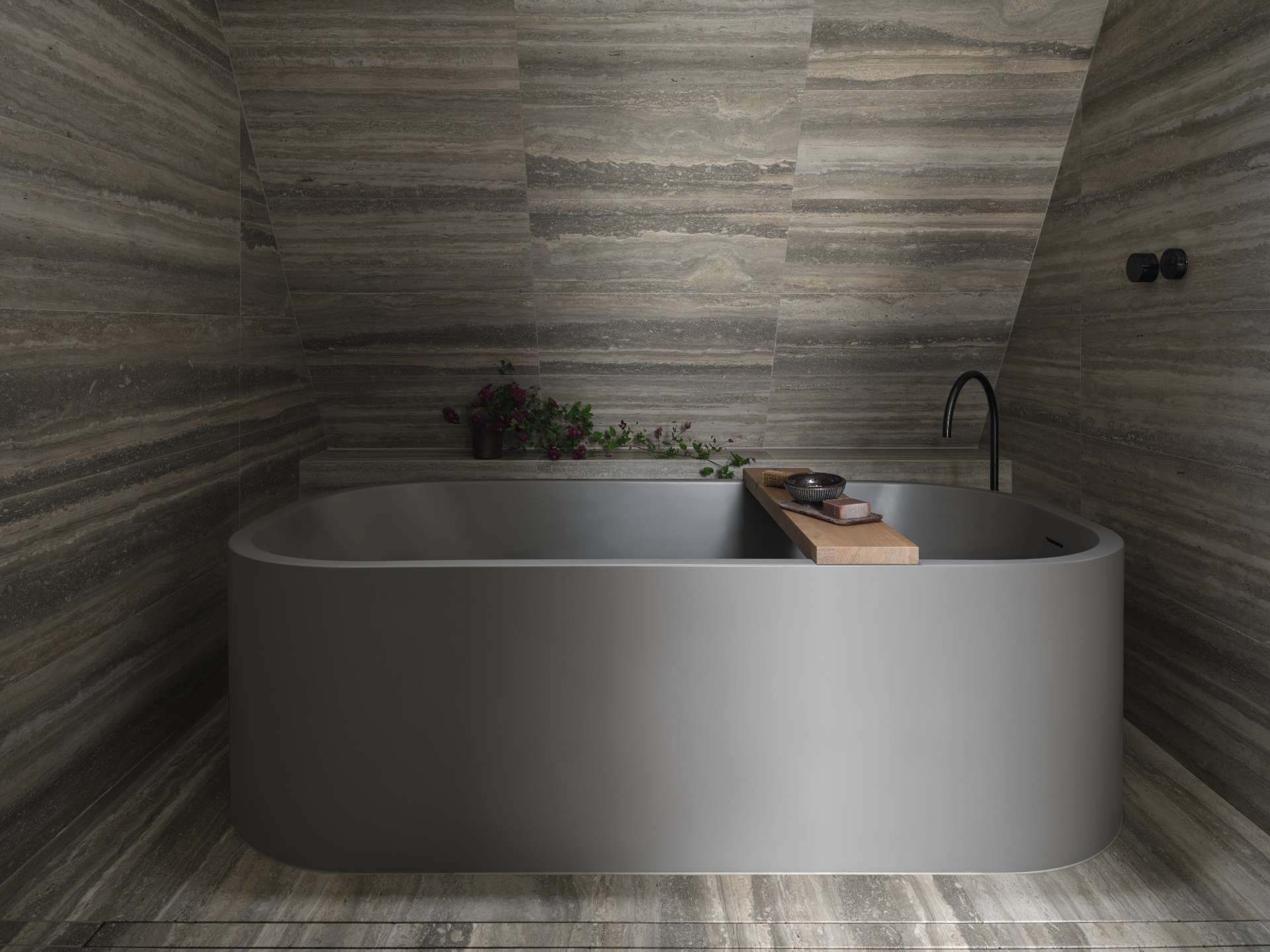 A modern bathroom with travertine walls and a freestanding modern grey bathtub.