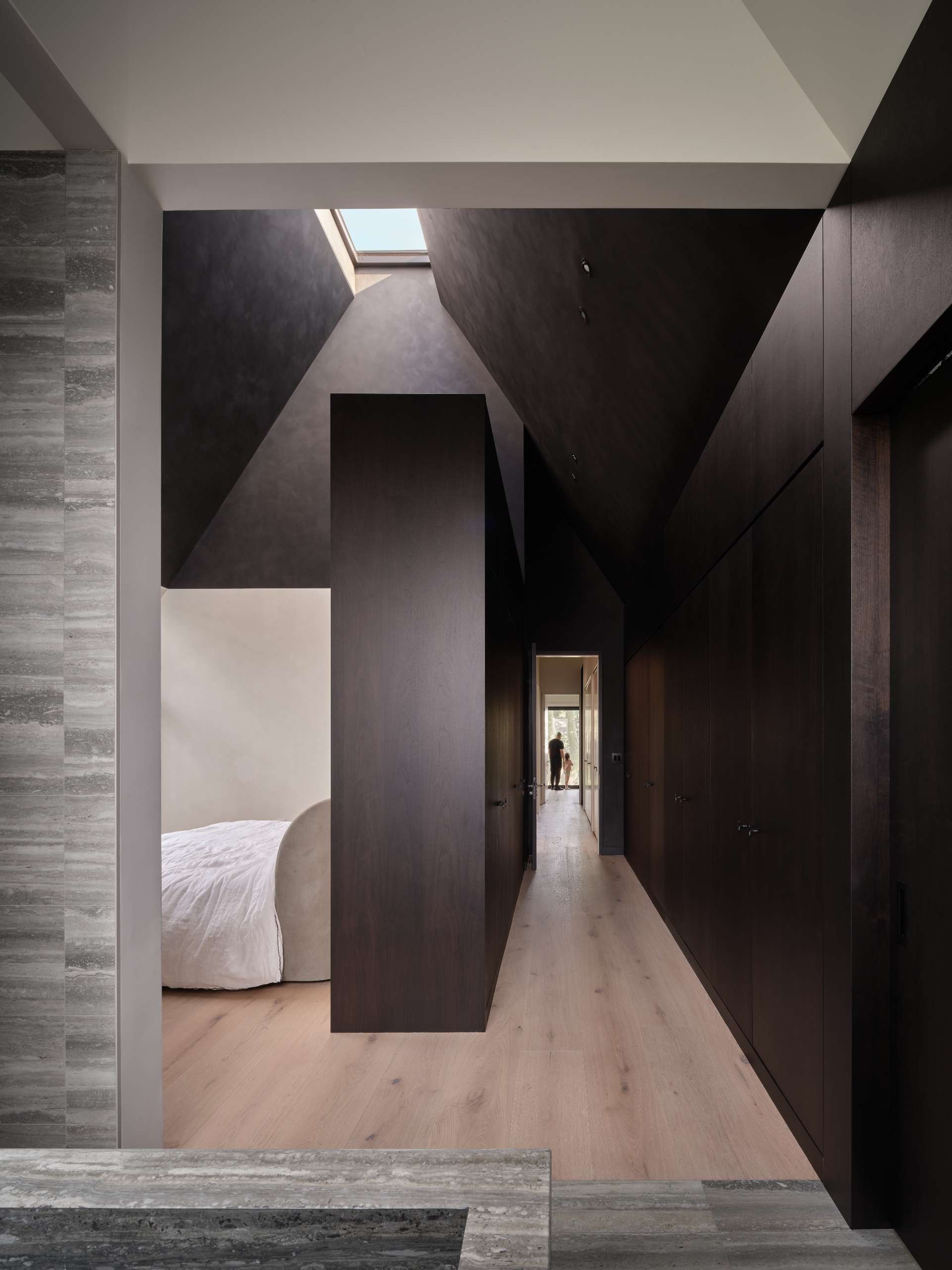 A modern primary suite with contrasting dark walnut and limestone walls.