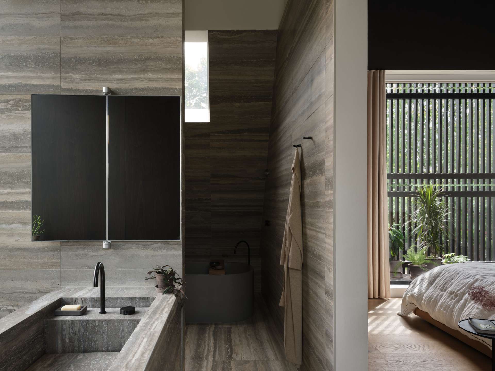 A modern ensuite bathroom with travertine walls and a freestanding modern grey bathtub.