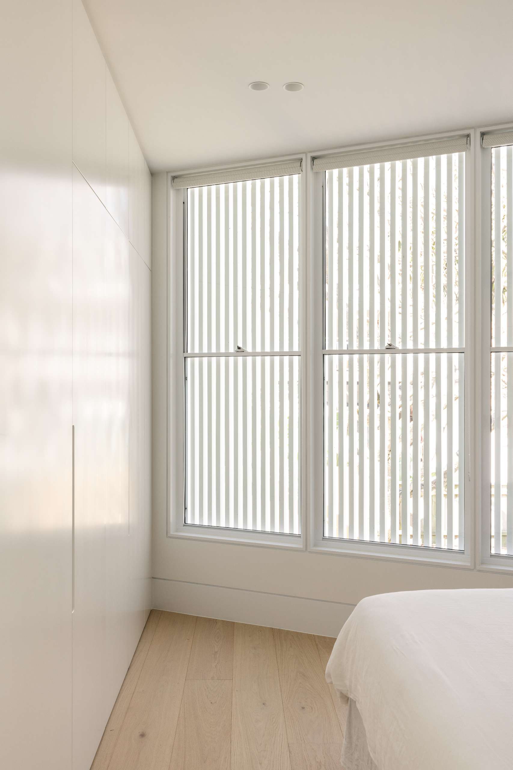 In the primary bedroom, a built-in wardrobe with flush cabinetry lines one wall, maintaining a clean and uncluttered look.