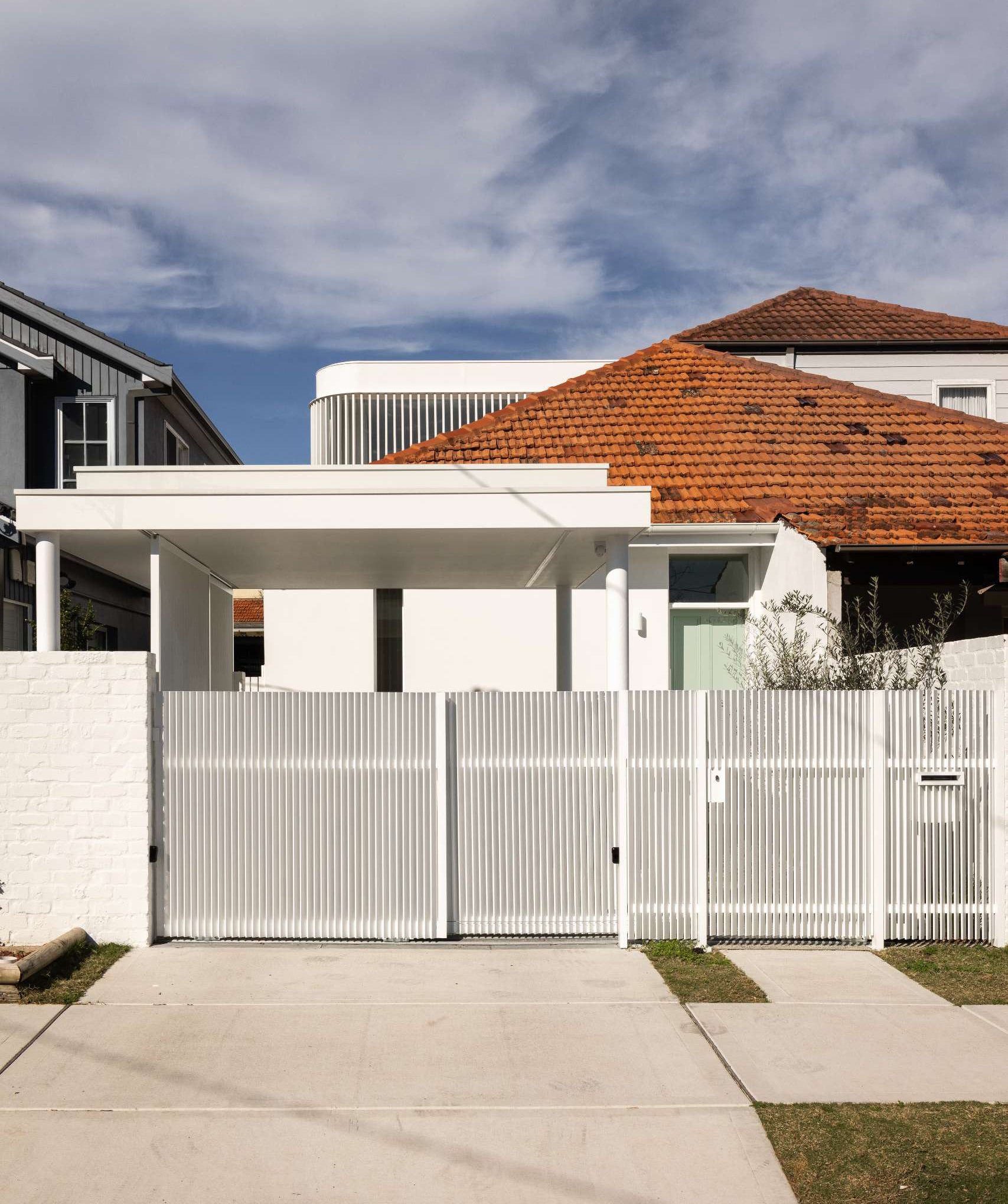 A dated brick facade received a modern refresh with crisp white render, minimalist lines, and vertical screening. The red tiled roof nods to the past, while a sleek carport and soft landscaping introduce the home's calm, contemporary style.