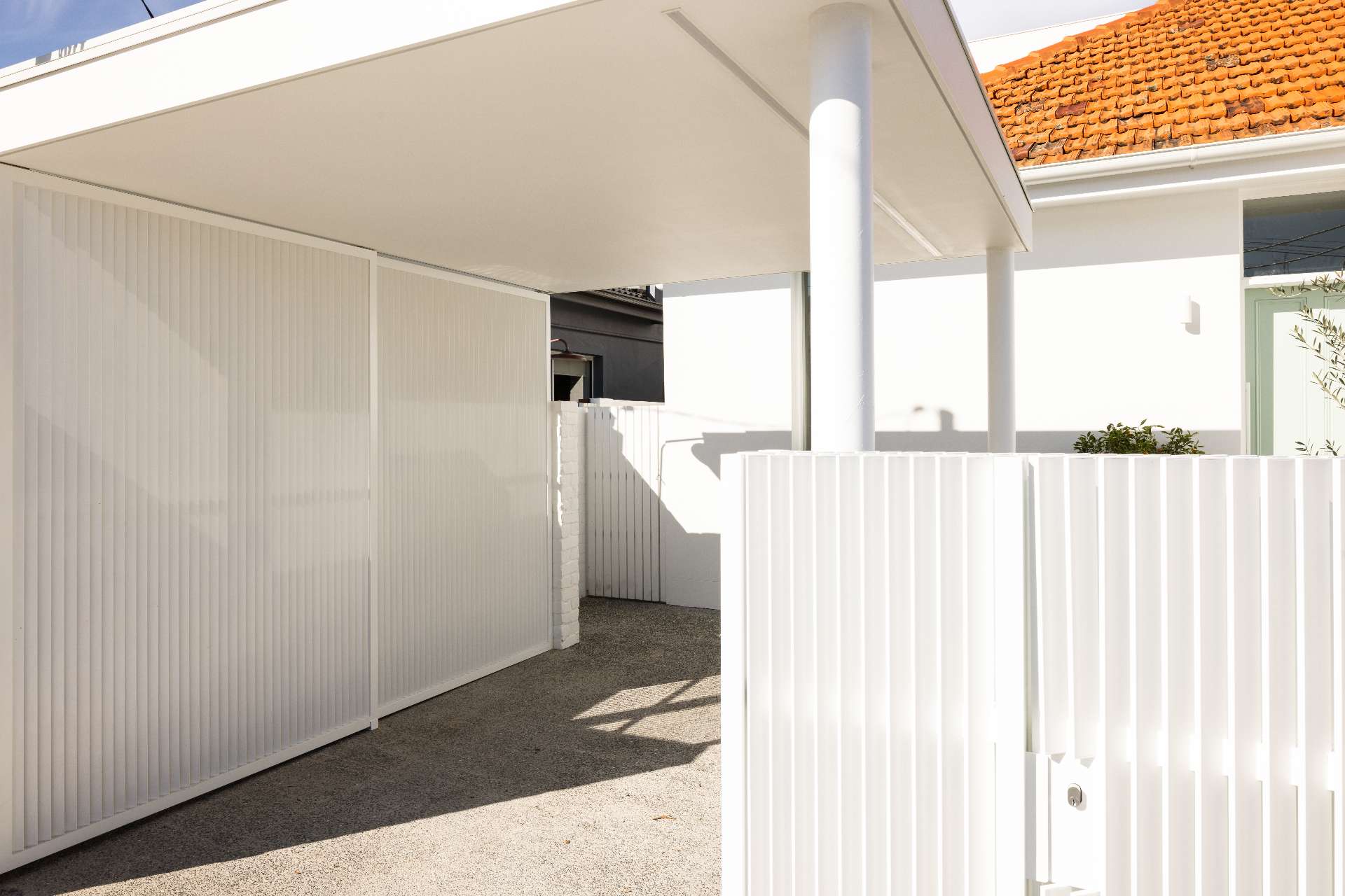 The original courtyard featured dated French doors, exposed utilities, and uneven paving. After the renovation, a sleek white facade, and fresh landscaping give the entry a serene, design-forward look. A pistachio green door complete the clean, coastal feel.