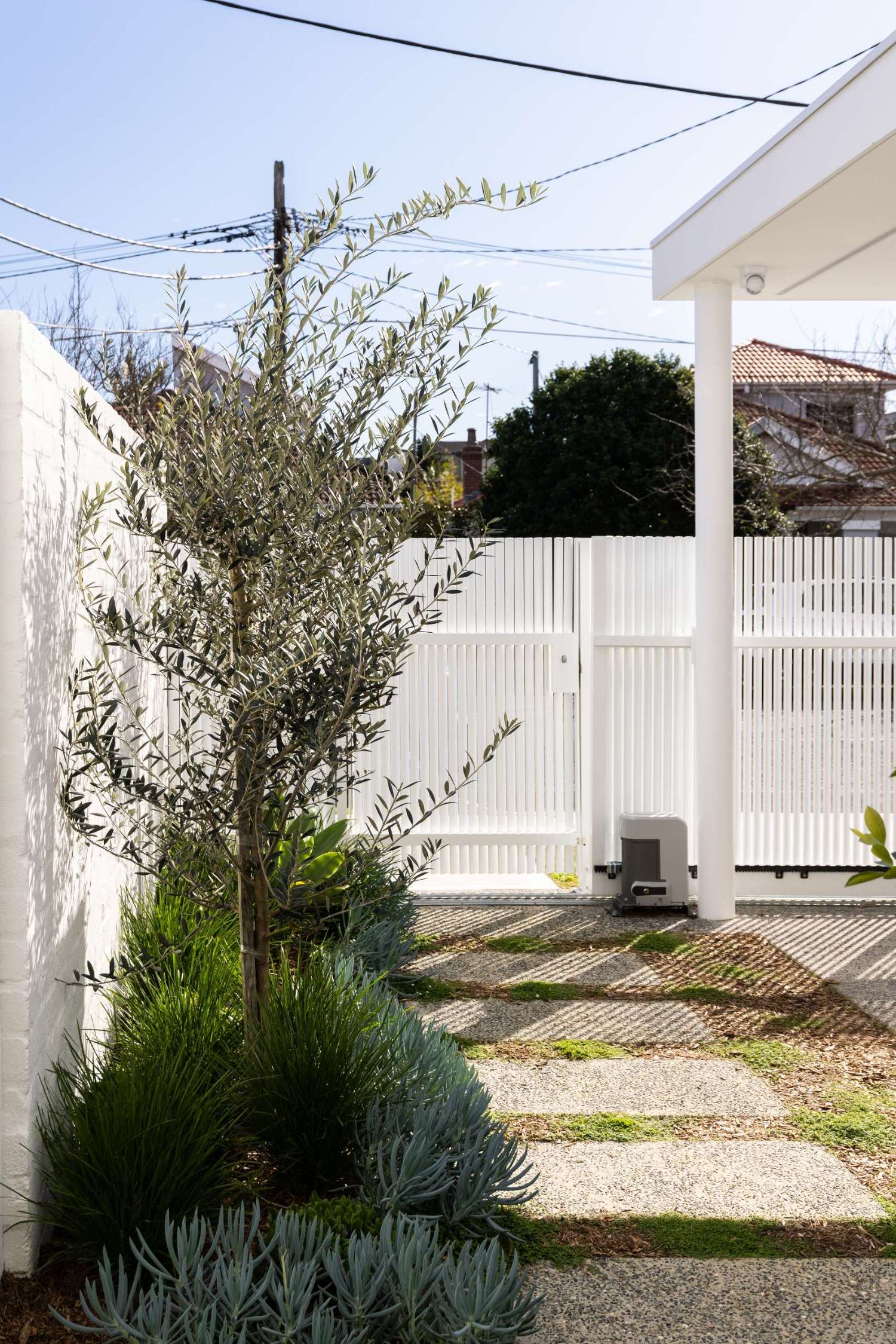 The original courtyard featured dated French doors, exposed utilities, and uneven paving. After the renovation, a sleek white facade, and fresh landscaping give the entry a serene, design-forward look. A pistachio green door complete the clean, coastal feel.