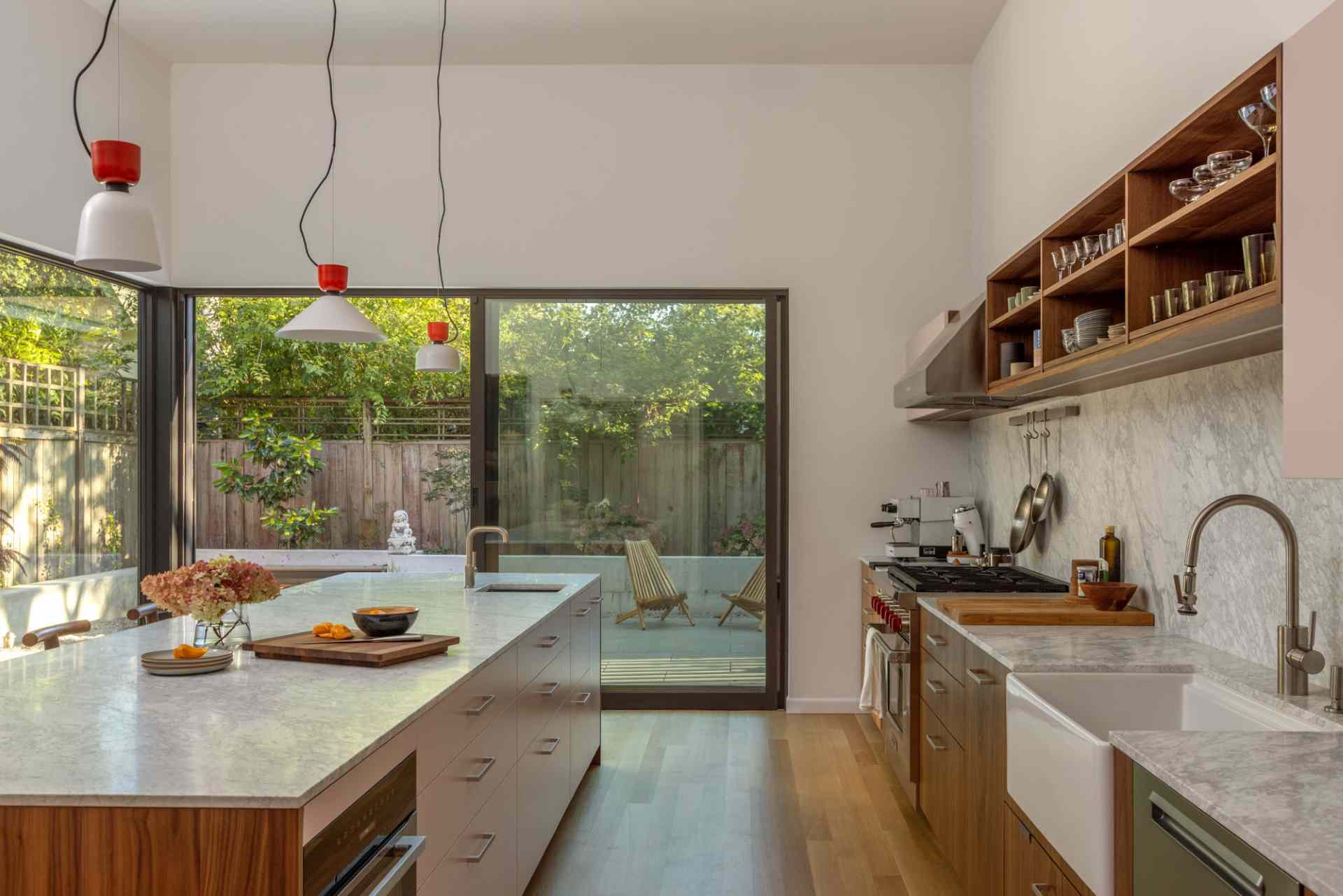 This modern kitchen opens to a small backyard with a concrete sitting wall, firepit, and outdoor cooking areas.