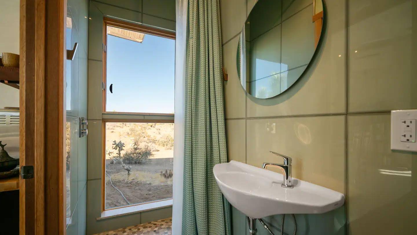 A small bathroom is discreetly tucked away in this desert cabin, with windows framing the views.