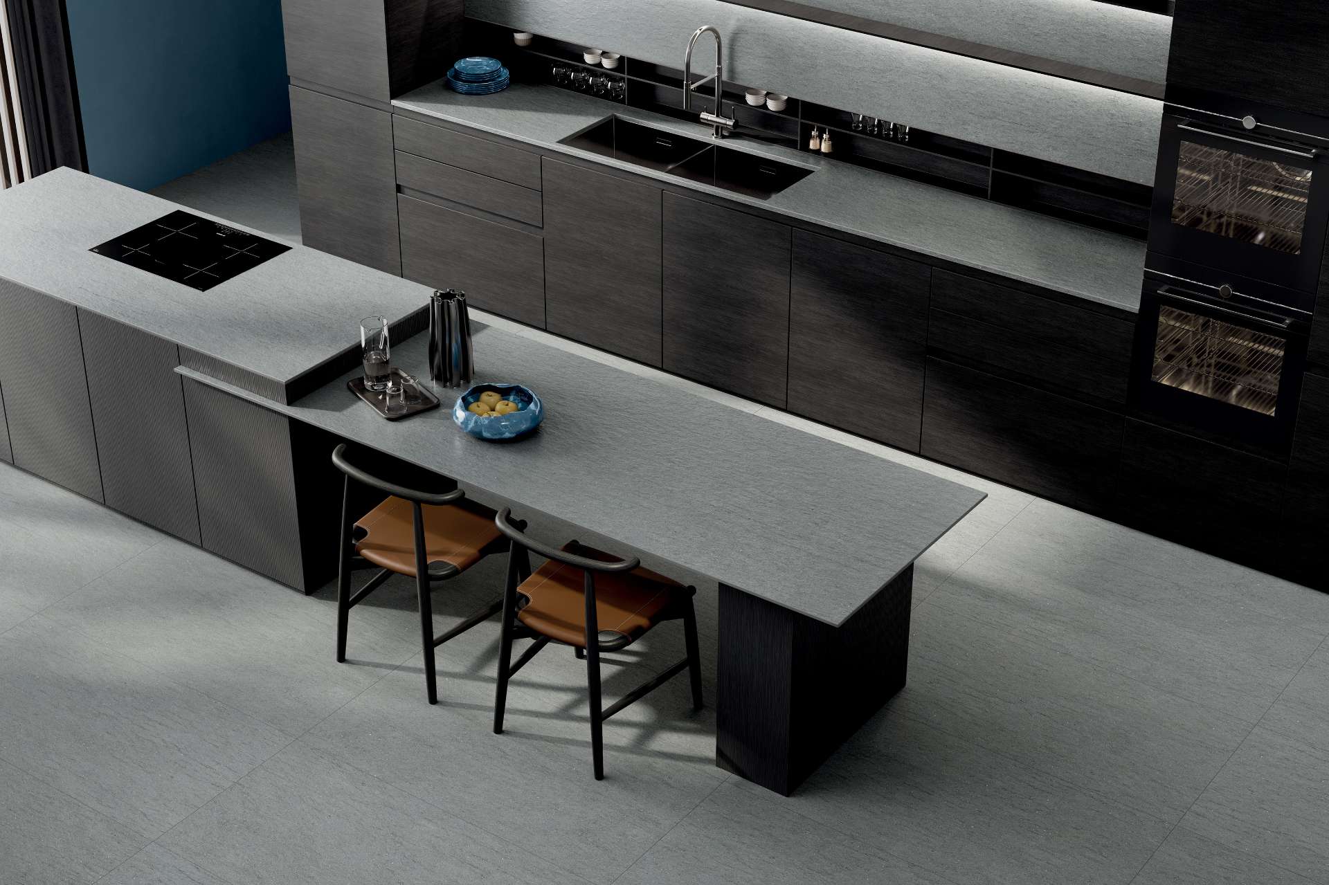 This modern kitchen pairs graphite-toned cabinetry with soft grey stone-look tile for a sleek, high-contrast design that feels both luxurious and grounded. Seating and clean lines create a space that’s as functional as it is striking.