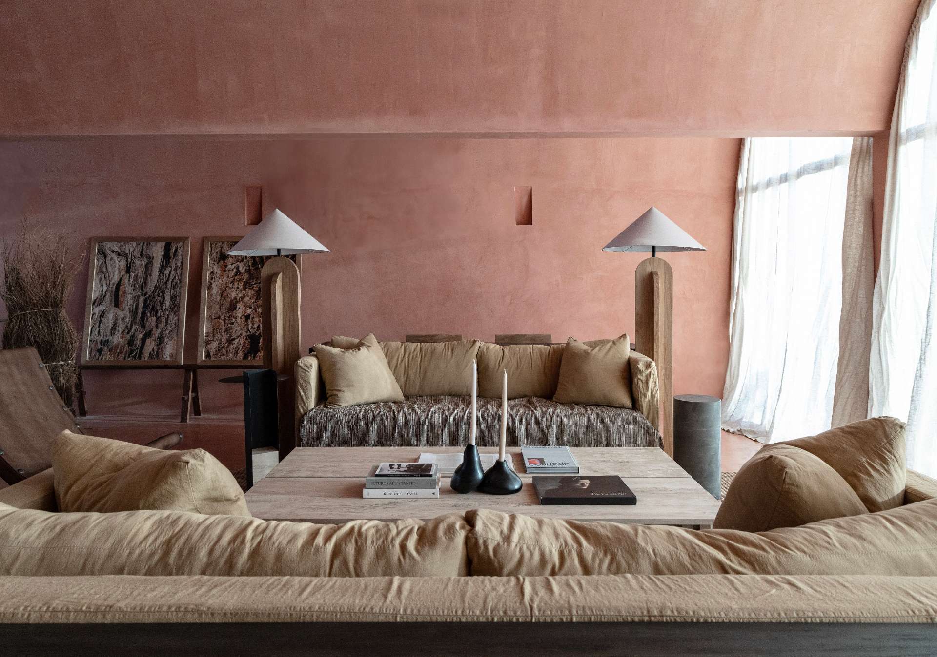 A serene, terracotta-toned living space showcases earthy textures, warm natural light, and a refined material palette. Walls in sunbaked hues form a calming backdrop for relaxed sofas, woven rugs, and solid wood furniture with primitive silhouettes.