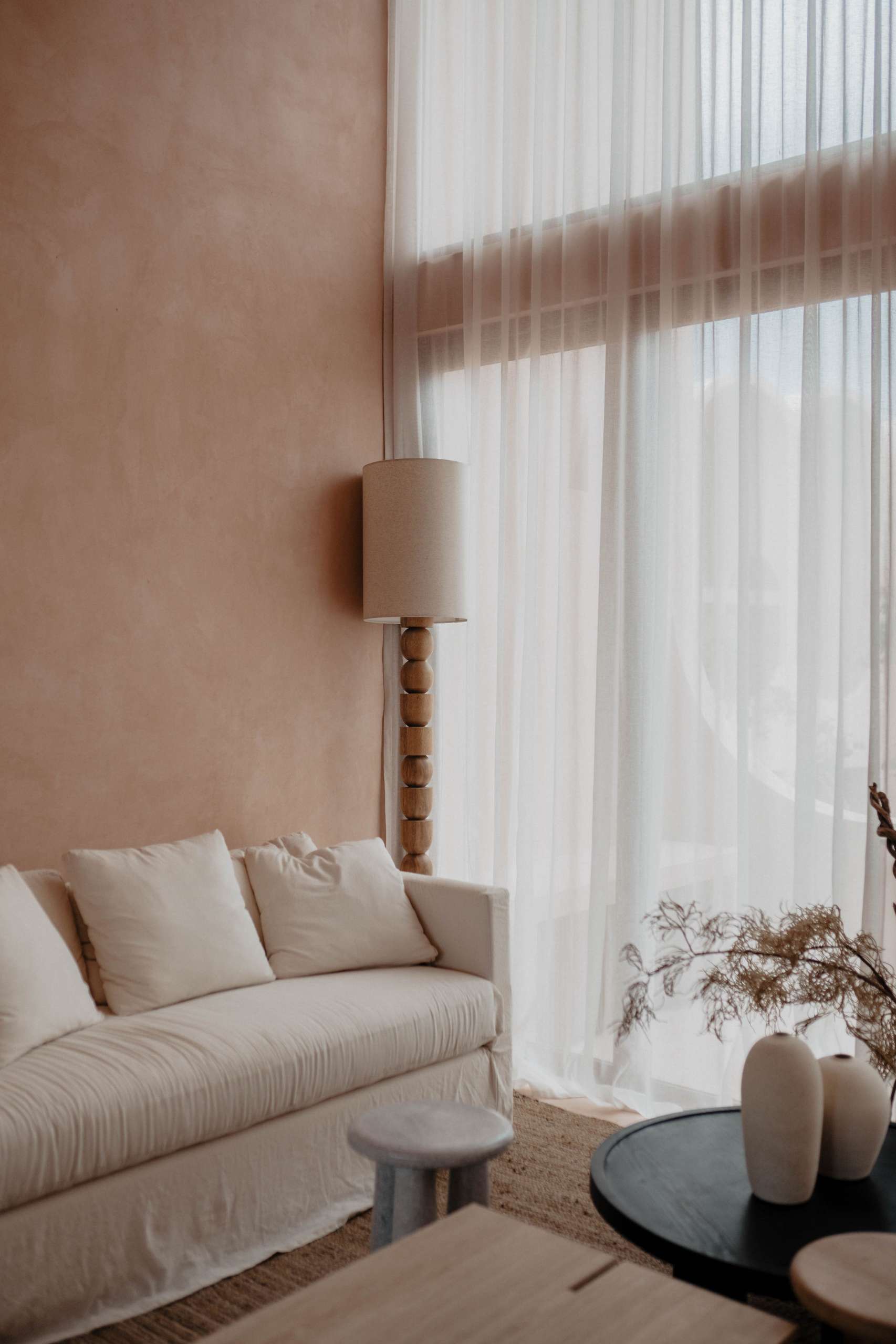 In this apartment, neutral tones and organic materials take center stage in the living room. Filtered sunlight washes over a minimalist sofa, sculptural wood tables, and a layered jute rug, creating a space that feels both serene and elemental.