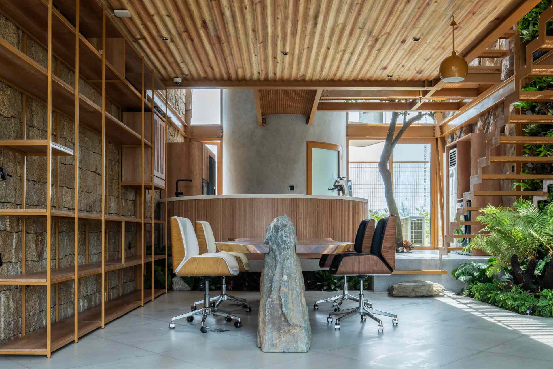 A structured meeting area combines sleek shelving with raw materials like stone and timber. Soft daylight and a green wall create a calm, inviting space that feels more like a retreat than a typical office.