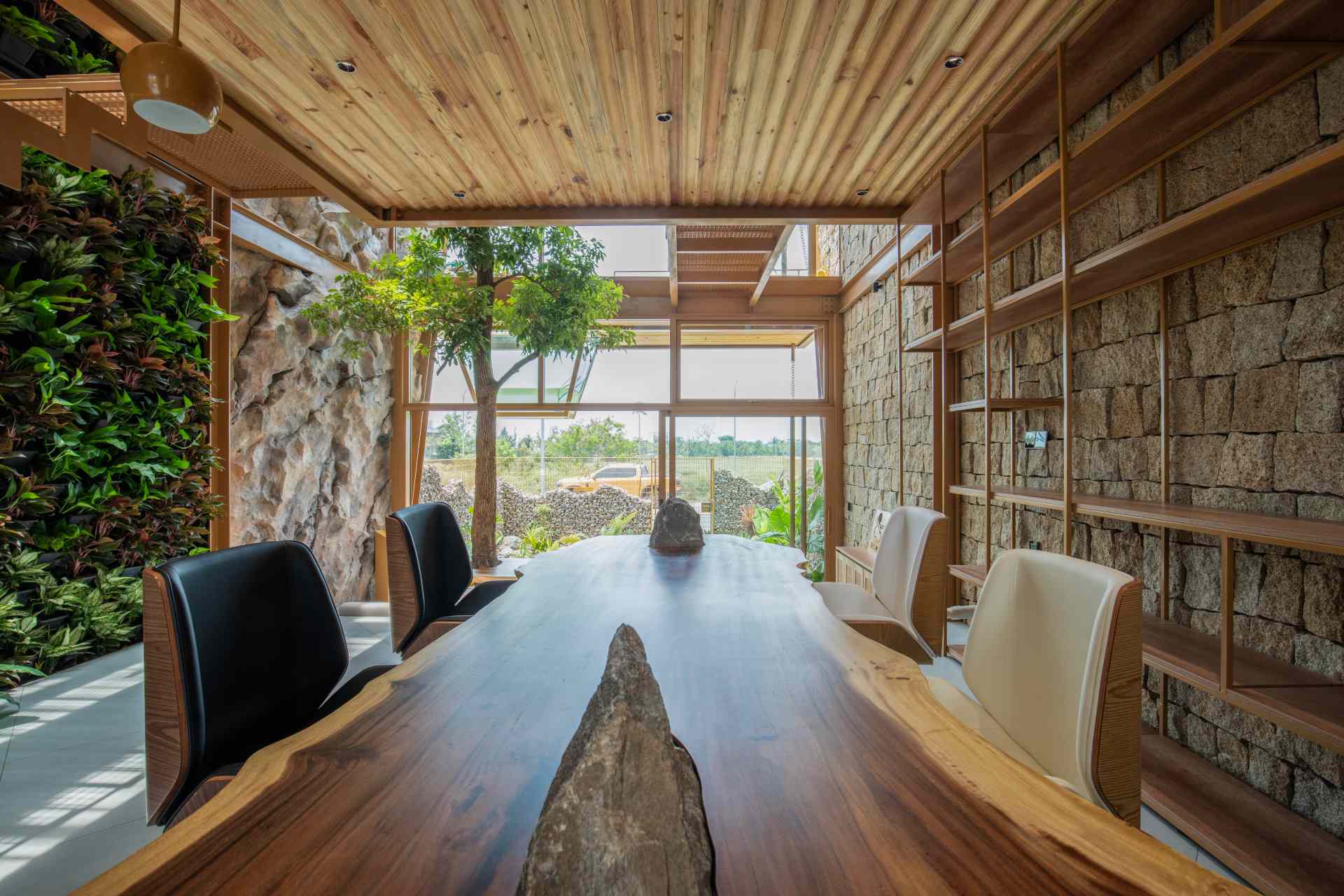 A structured meeting area combines sleek shelving with raw materials like stone and timber. Soft daylight and a green wall create a calm, inviting space that feels more like a retreat than a typical office.