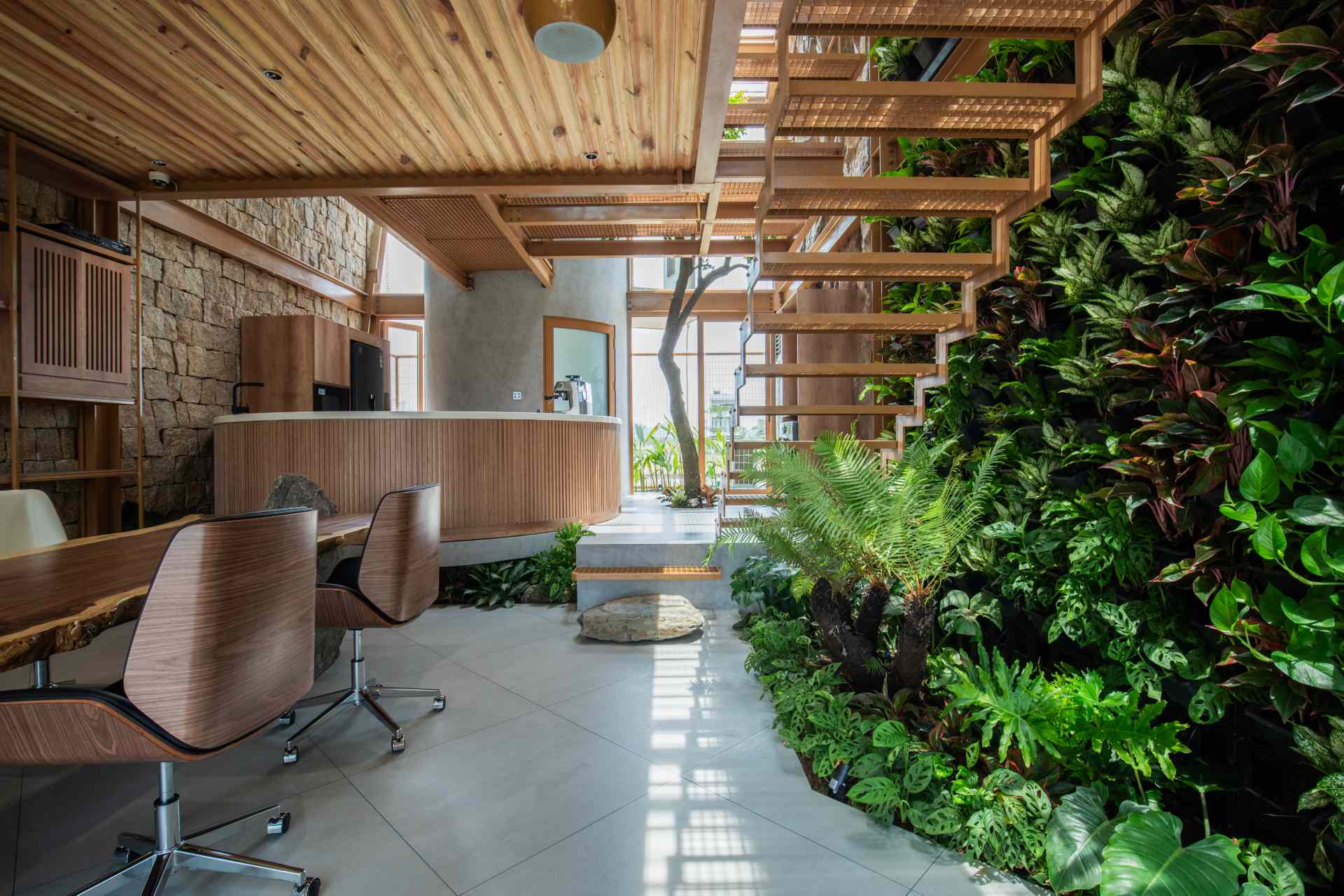 A structured meeting area combines sleek shelving with raw materials like stone and timber. Soft daylight and a green wall create a calm, inviting space that feels more like a retreat than a typical office.