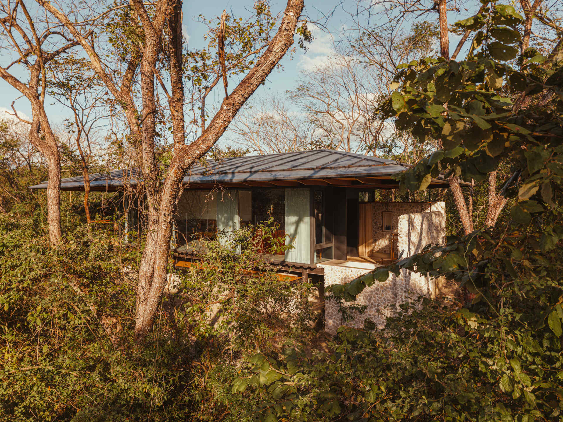 A stone, wood, and glass clad jungle bungalow in Costa Rica blends effortlessly into its forest surroundings.