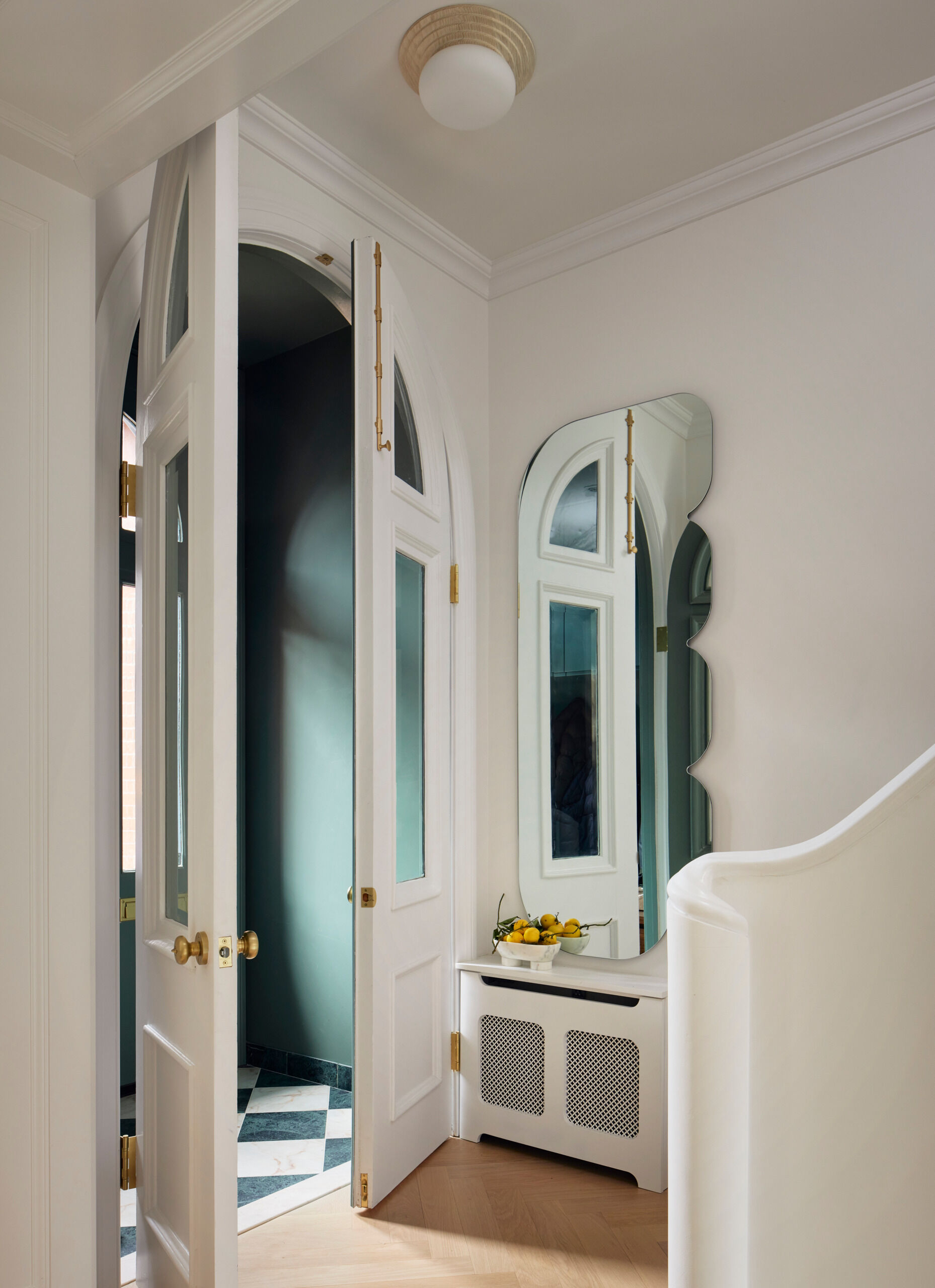 This entry makes a strong first impression with walls painted in a rich green, playing off a playful green and pink checkerboard tile floor, a fresh twist on the traditional. A custom asymmetrical mirror echoes the curved arch of the original doorway, setting the tone for the sculptural language that continues throughout the house.