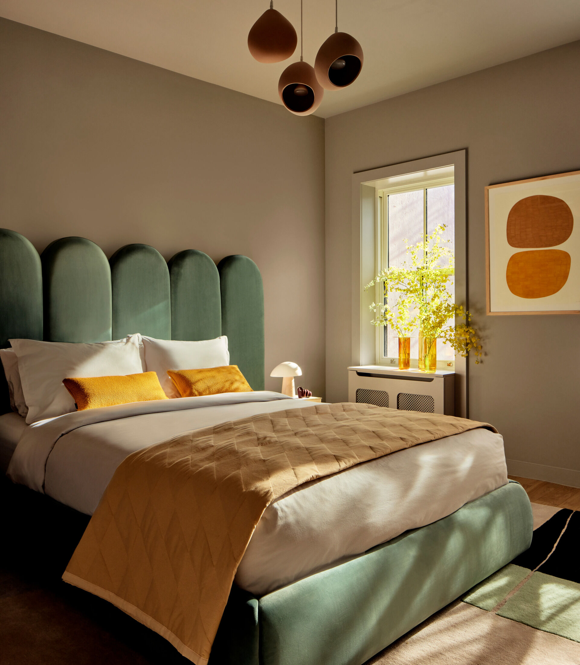 This guest bedroom makes a bold statement with a green velvet bed set between custom travertine side tables, while artwork, a wool rug, and trio of clay pendants bring warmth and texture.