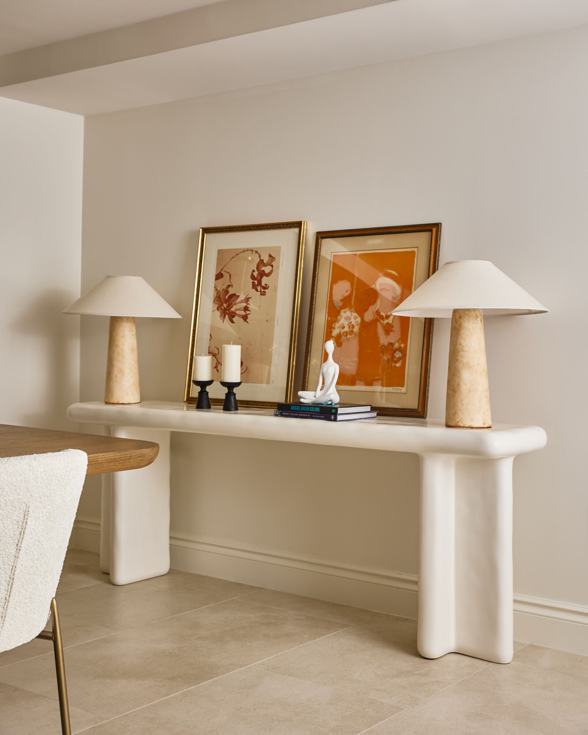 A sculptural white console and sandy stone lamps bring warmth and texture to this modern dining room corner. Terracotta artwork and personal touches like books and a figurine add relaxed, curated charm.