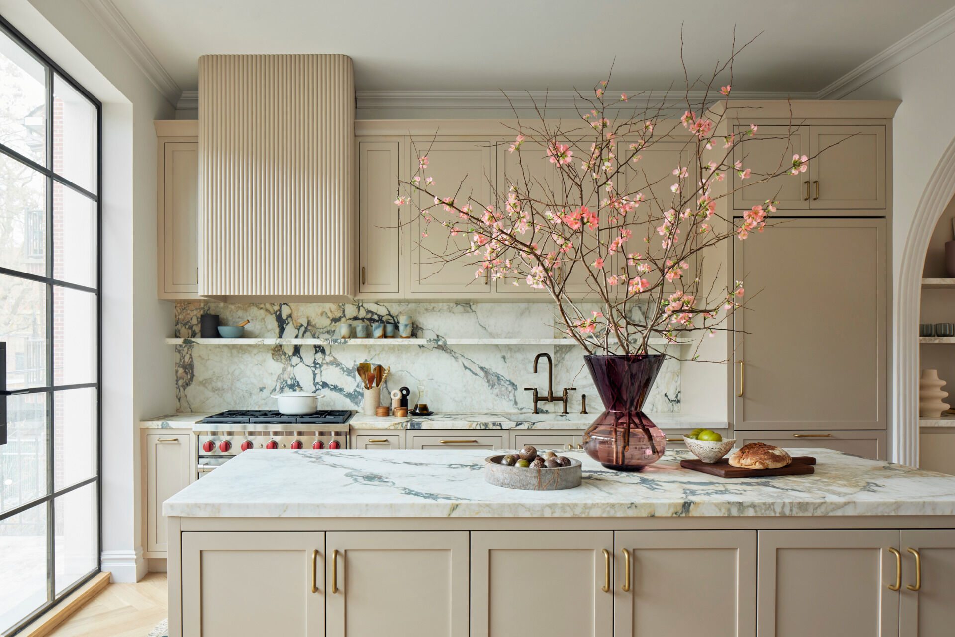 The kitchen is grounded by Calacatta Vagli Viola marble countertops and an island painted in warm mushroom tones. Custom cabinetry and a curved pantry bring softness to the architecture, while a trio of hand-blown glass pendants hang above a pale oak dining table. It’s an inviting space that balances simplicity with elegance, ready for casual meals or larger gatherings.