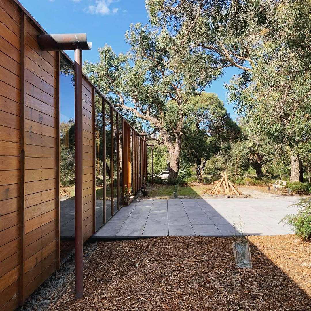 A recycled timber home and studio built with passive solar principles and reclaimed materials. It features two pavilions, full-height glazing, and a bluestone terrace set beneath native trees.