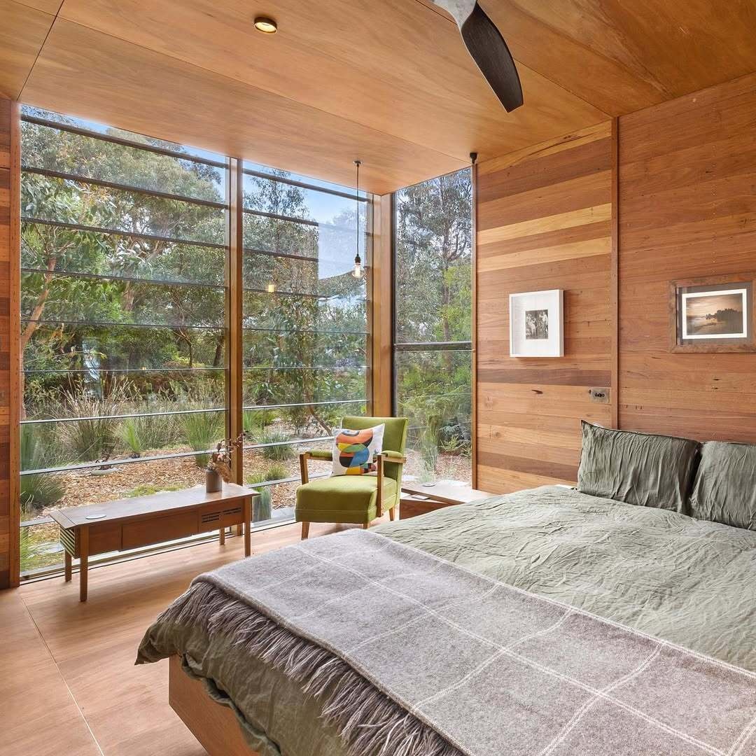 Full-height glazing connects this bedroom with wood walls, to the surrounding landscape, while passive orientation ensures comfort across seasons. The minimal footprint supports a lifestyle focused on essentials and experience over excess.