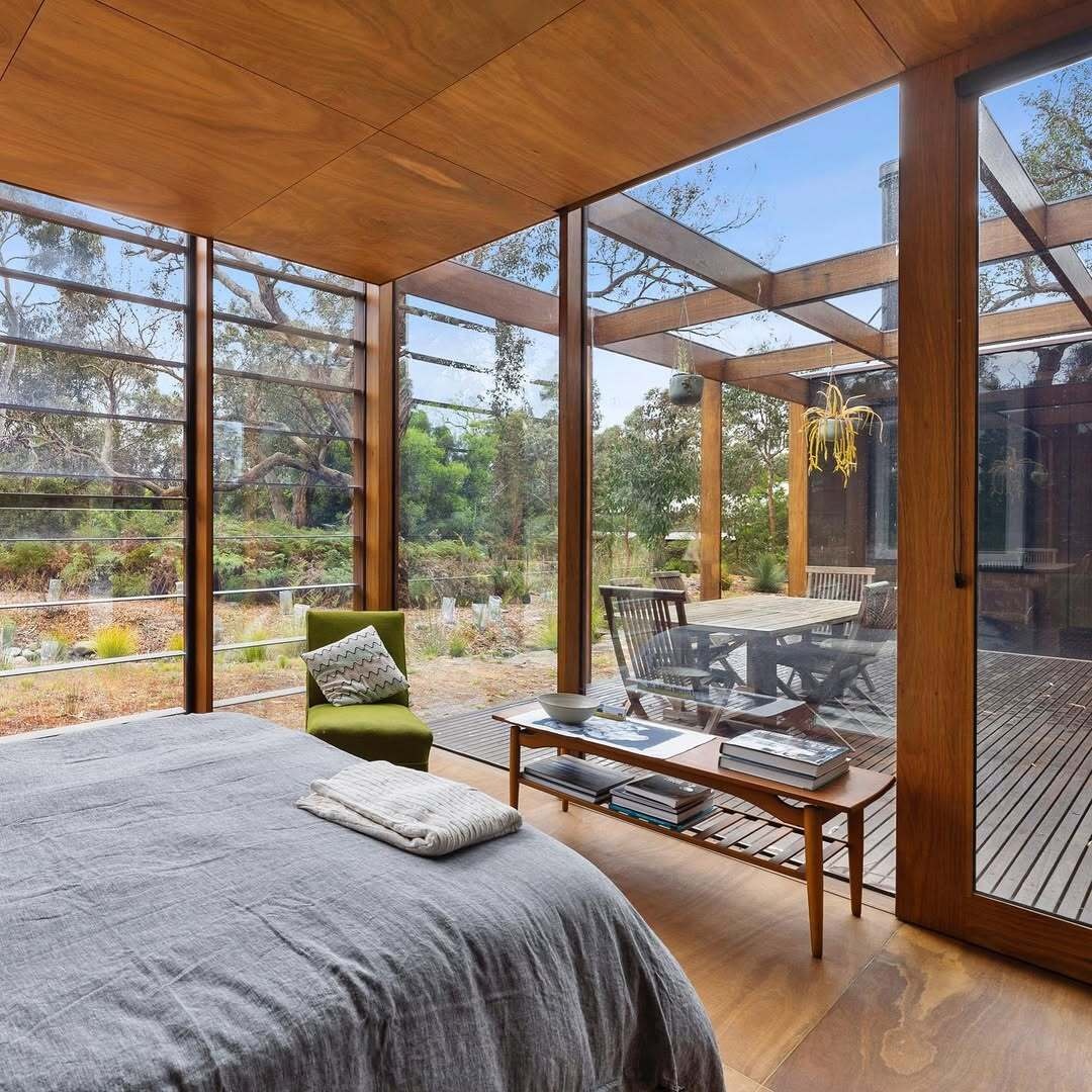 Full-height glazing connects this bedroom with wood walls, to the surrounding landscape, while passive orientation ensures comfort across seasons. The minimal footprint supports a lifestyle focused on essentials and experience over excess.