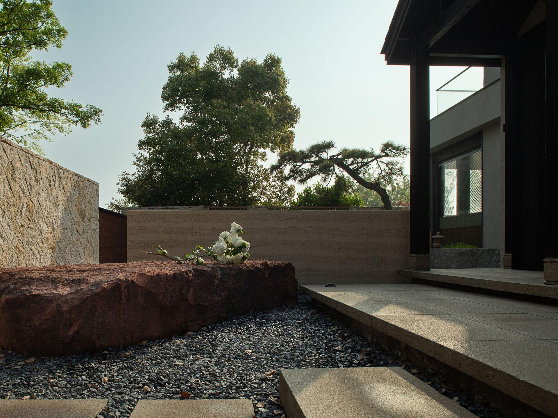 A bold red stone anchors the front courtyard, its raw surface contrasting with the smooth, pale walkway that leads to the home.
