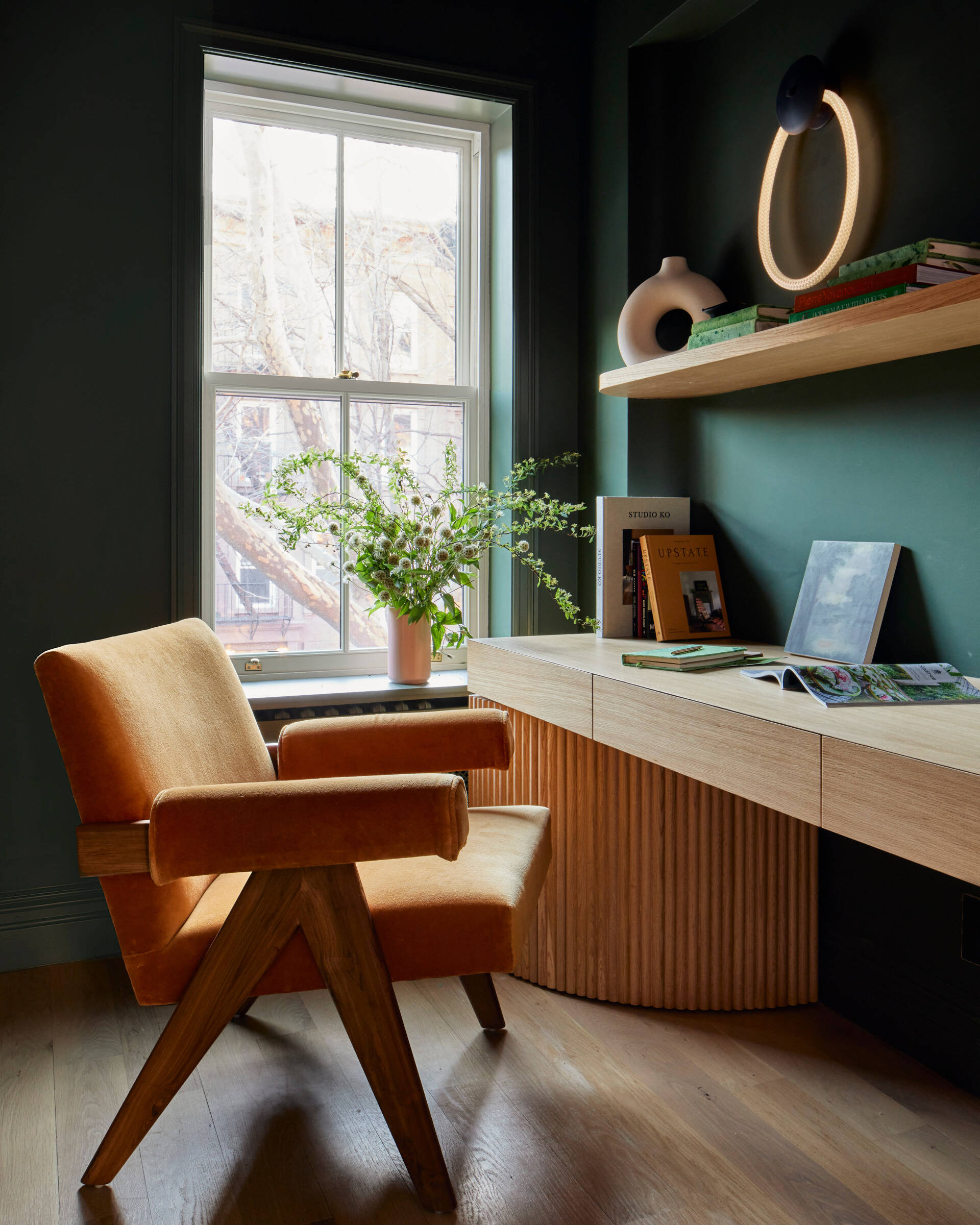 This home office is cloaked in deep forest green and features a custom tambour white oak desk. LED lighting and window illuminates the space, balancing moodiness with functionality.