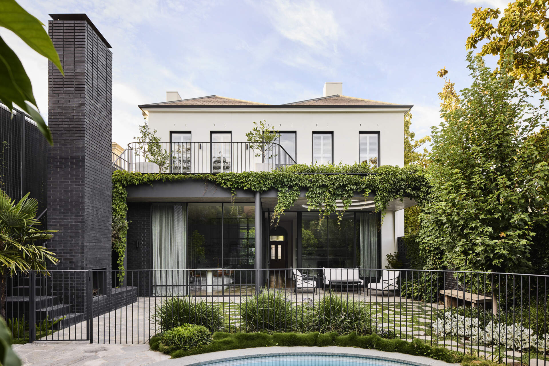 A defining feature of the rear of this remodeled home is a courtyard with a large circular cut-out overhead, a bold geometric move that invites sky views and dappled sunlight into the space below. Positioned above the outdoor dining area, the cut-out frames the moment, turning the patio into more than just a transitional space.