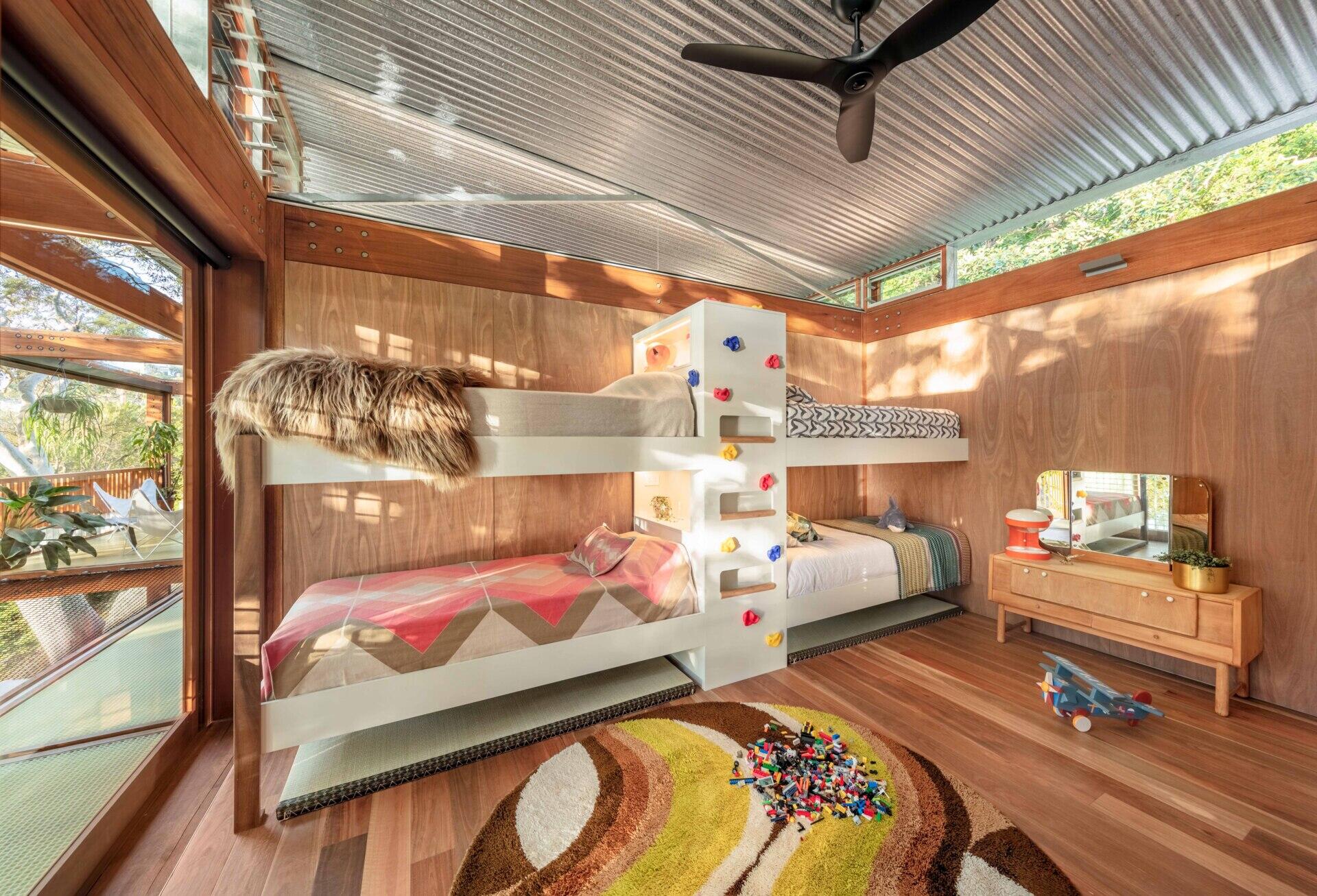 This kids’ bedroom is playful but simple. Built-in bunk beds with a mini rock climbing wall and ladder, create cozy corners for sleep or reading, while timber walls and floors keep it connected to the rest of the home.
