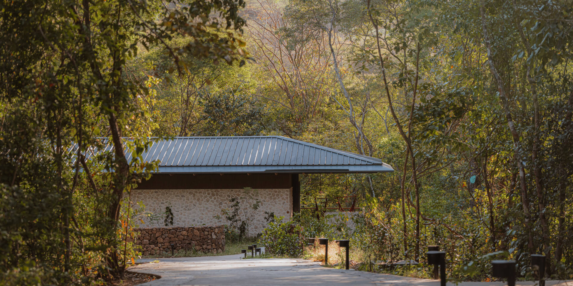 A stone-clad jungle bungalow in Costa Rica blends effortlessly into its forest surroundings. A curved concrete path leads to the entrance, while a floating terrace and rich timber ceiling invite guests into a space that feels both grounded and elevated.