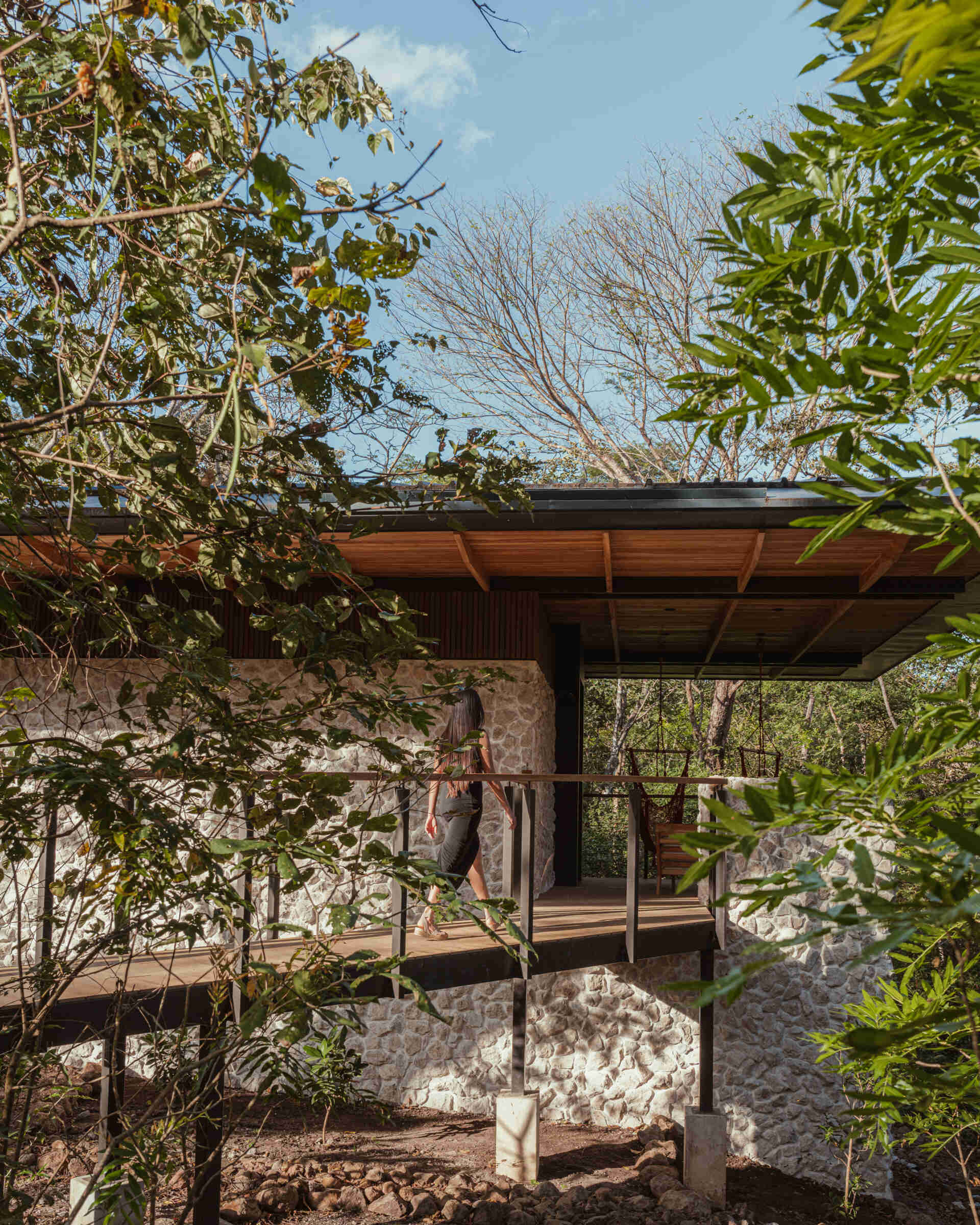 A raised walkway leading to a stone bungalow nestled in the Costa Rican forest. Elevated on slender pilotis, the structure floats above the ground, blending tropical modern design with lush, natural surroundings.