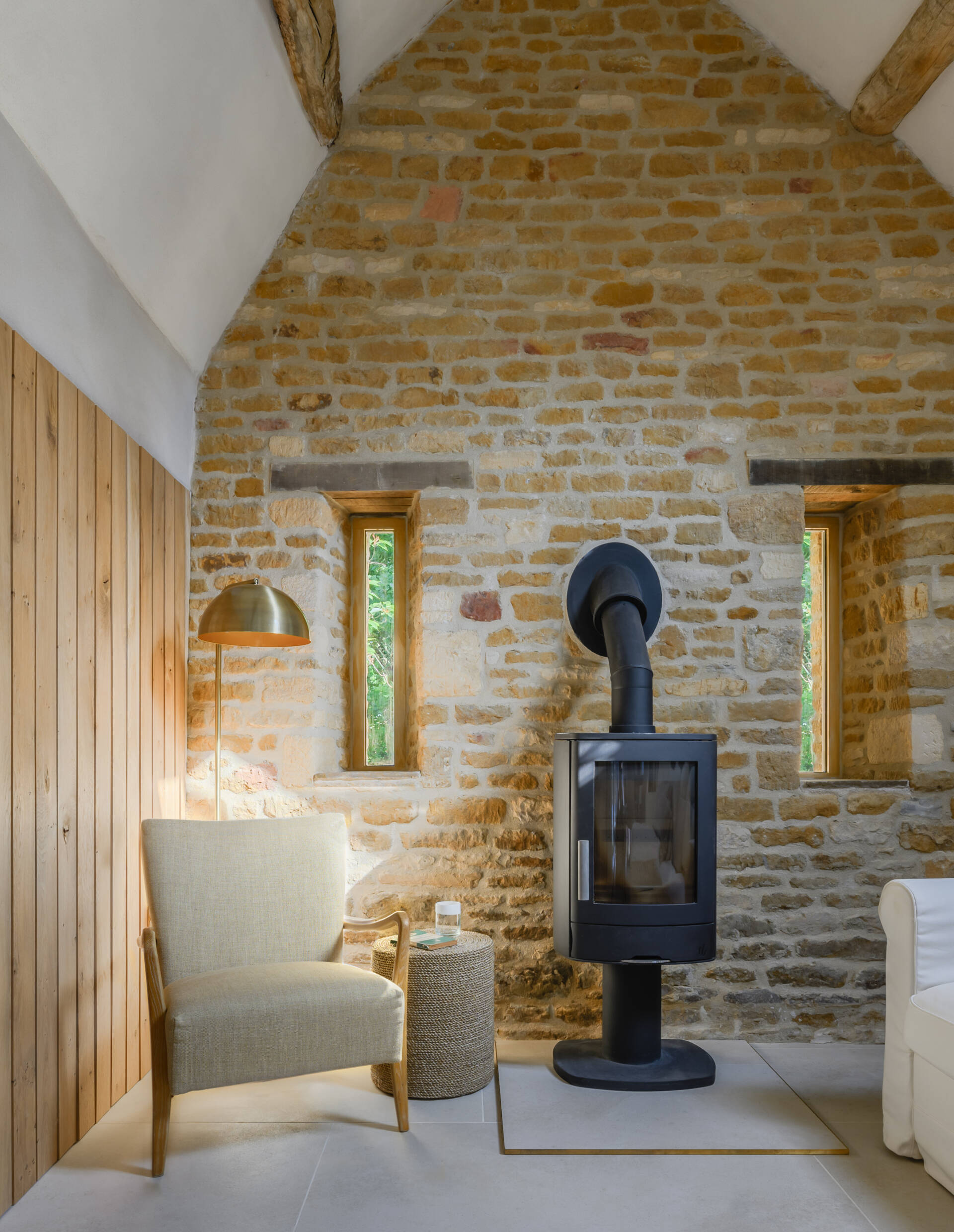 The main living space of this renovated cowshed is understated and relaxed, with a focus on texture rather than decoration. Exposed timber beams run across the living area, adding depth and authenticity to the otherwise minimal interior. Their weathered texture contrasts gently with the raw lime plaster and clean lines of the new insertions. Rather than conceal or restore them too much, the beams were left largely untouched, allowing the marks of time to remain visible and grounding the space in its agricultural past.
