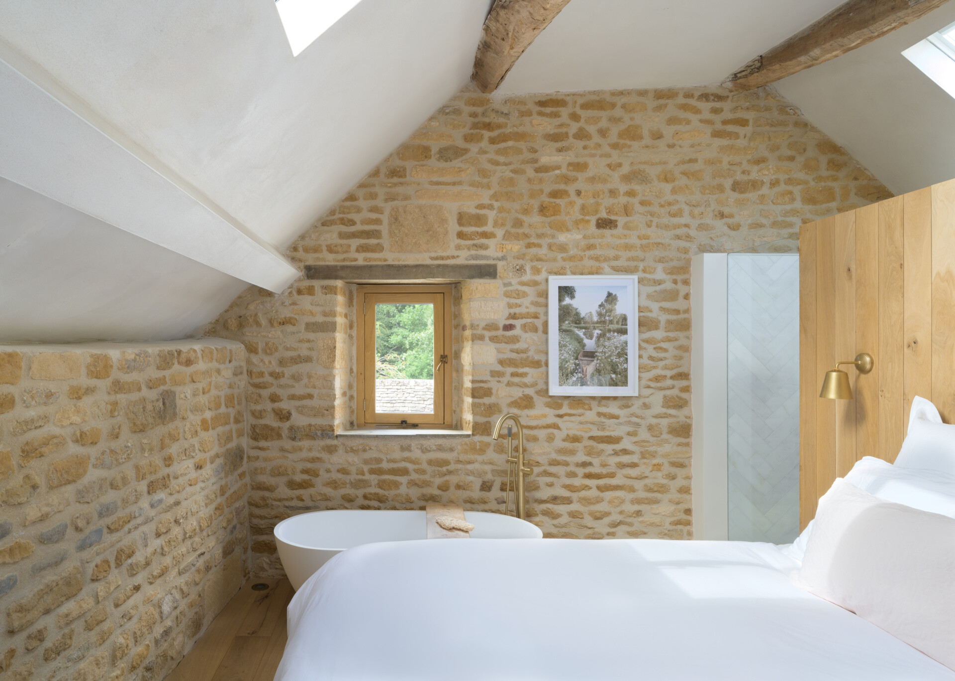 In a former hayloft, the primary suite is compact yet full of character. The freestanding bathtub is located by the bed, while the remaining areas of the bathroom are cleverly tucked under the eaves, making the most of the available space. A shower is even suspended over the stair void, a detail that speaks to the creative problem-solving throughout the project.