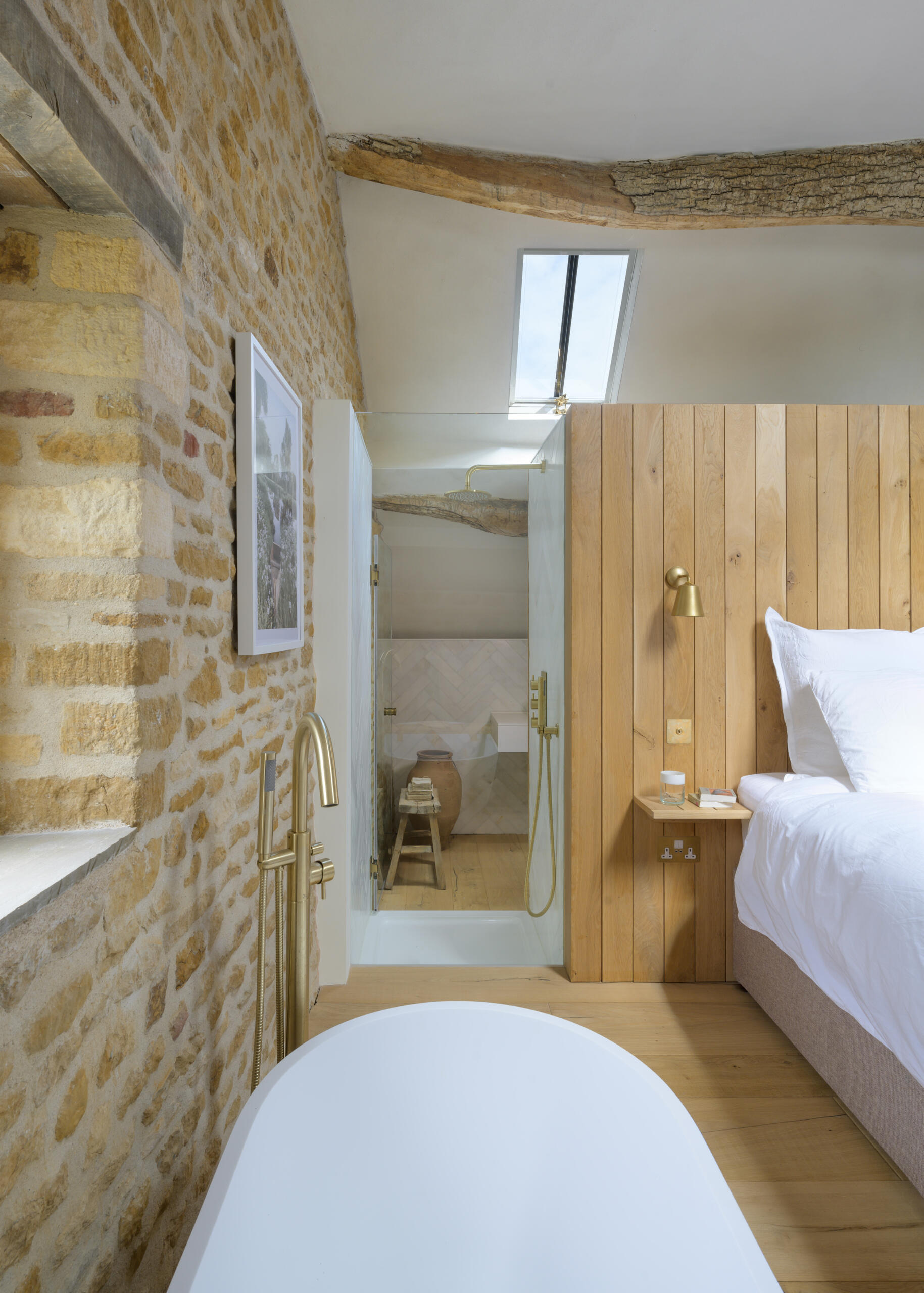 In a former hayloft, the primary suite is compact yet full of character. The freestanding bathtub is located by the bed, while the remaining areas of the bathroom are cleverly tucked under the eaves, making the most of the available space. A shower is even suspended over the stair void, a detail that speaks to the creative problem-solving throughout the project.