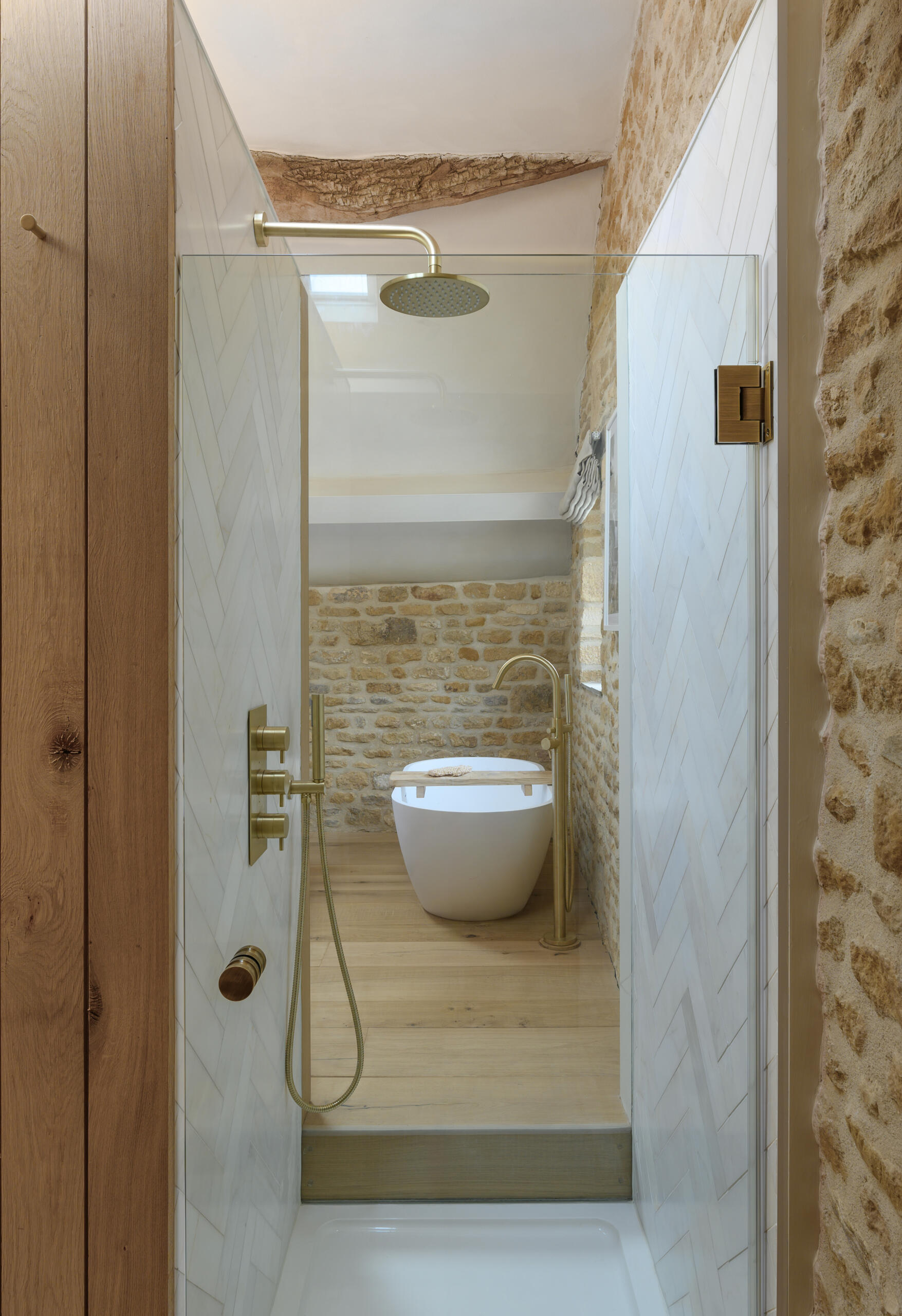 In a former hayloft, the primary suite is compact yet full of character. The freestanding bathtub is located by the bed, while the remaining areas of the bathroom are cleverly tucked under the eaves, making the most of the available space. A shower is even suspended over the stair void, a detail that speaks to the creative problem-solving throughout the project.