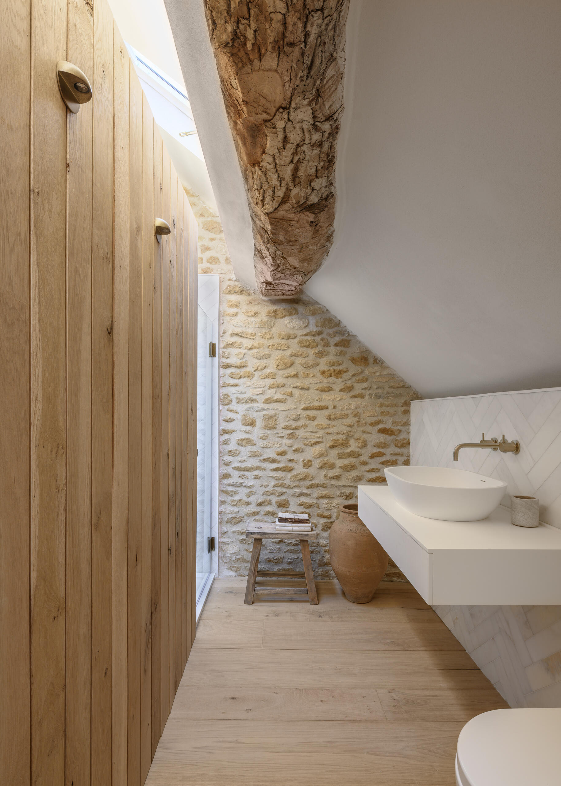 In a former hayloft, the primary suite is compact yet full of character. The freestanding bathtub is located by the bed, while the remaining areas of the bathroom are cleverly tucked under the eaves, making the most of the available space. A shower is even suspended over the stair void, a detail that speaks to the creative problem-solving throughout the project.