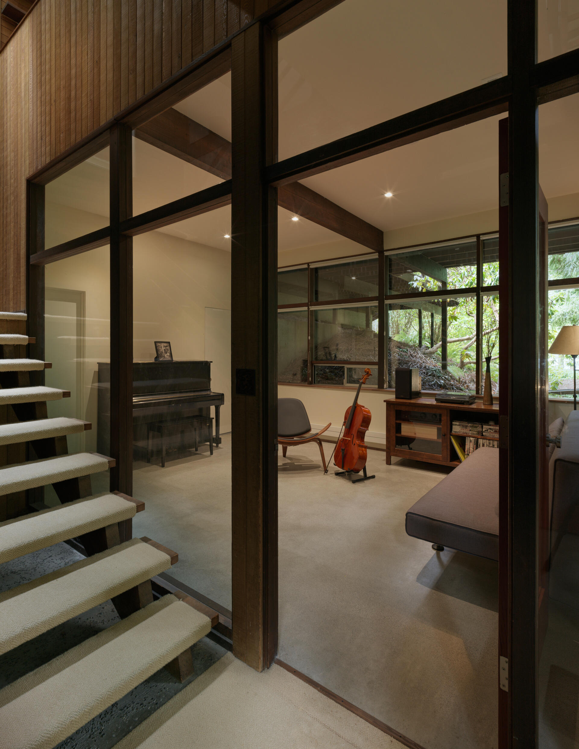 Once a studio for Alden Mason, this creative corner of the Mid-Century Modern home now serves as a music room. Nearby, the open-tread stairs rise through sunlight beneath a bold Rauschenberg print.