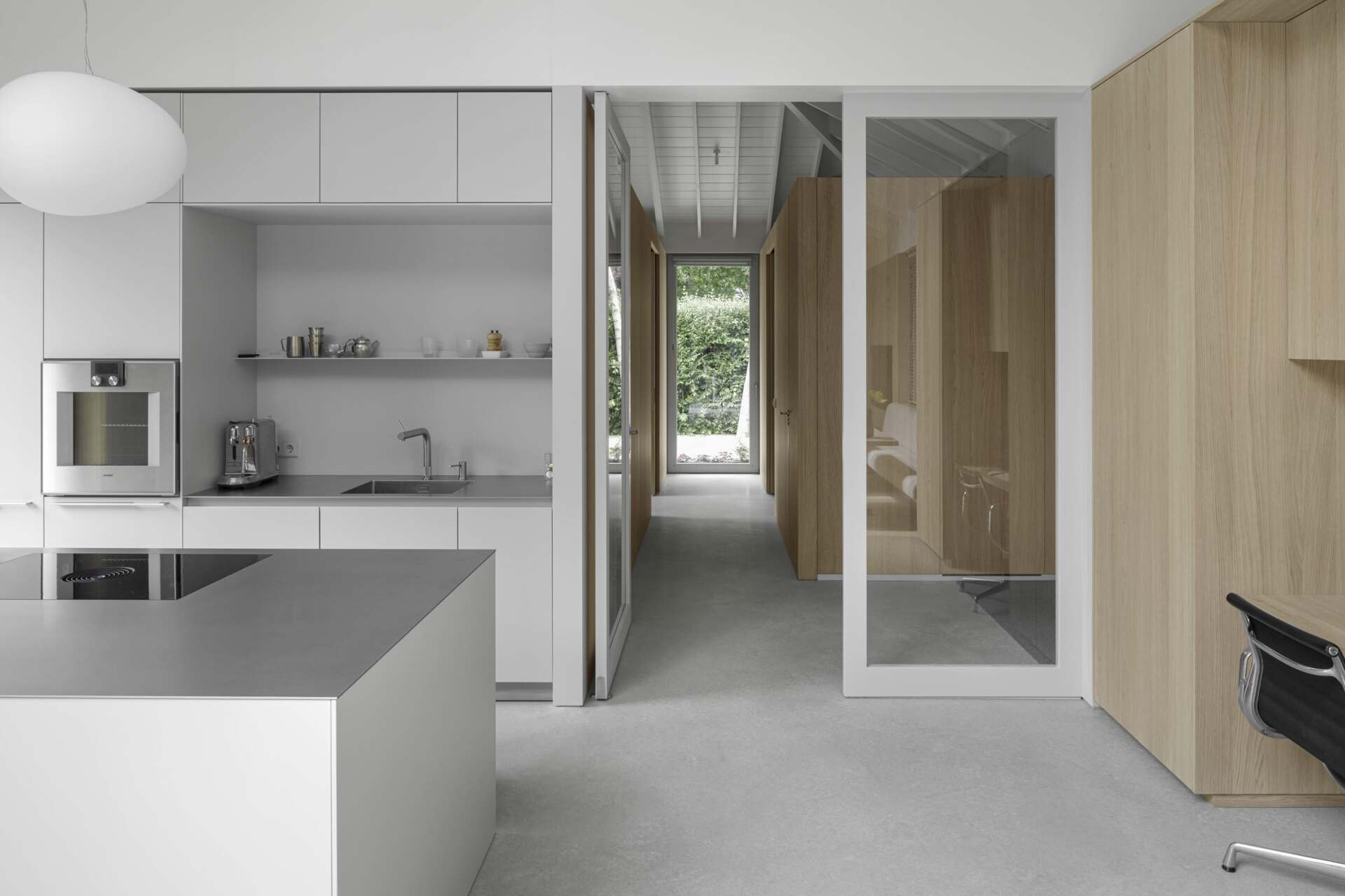 This kitchen includes minimalist hardware-free cabinetry that complements the surrounding wall panels, with horizontal lines that draw the eye and enhance the feeling of space. Its placement alongside the patio offers a unique indoor-outdoor flow, allowing the kitchen to extend into the garden during warmer months.