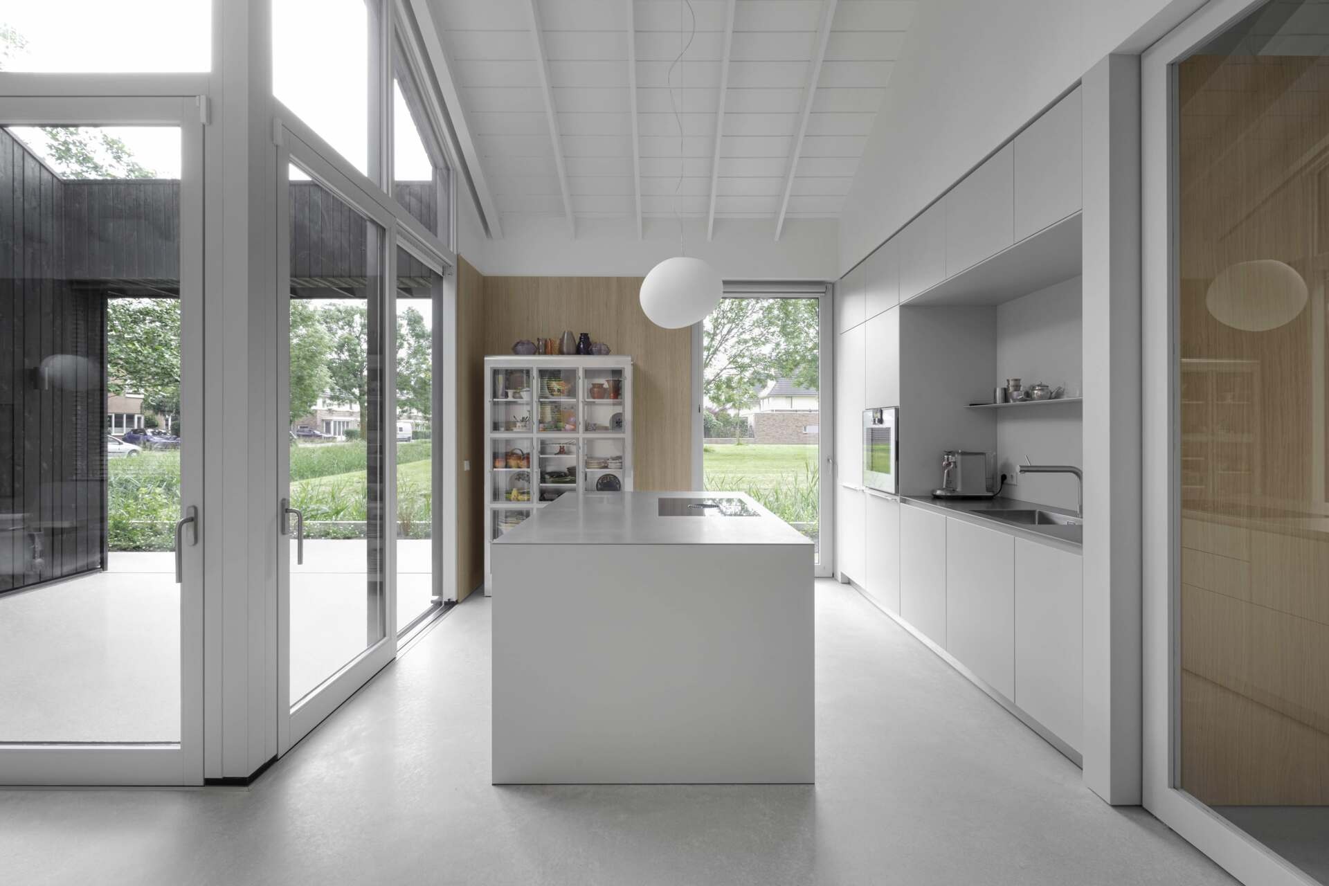 This kitchen includes minimalist hardware-free cabinetry that complements the surrounding wall panels, with horizontal lines that draw the eye and enhance the feeling of space. Its placement alongside the patio offers a unique indoor-outdoor flow, allowing the kitchen to extend into the garden during warmer months.