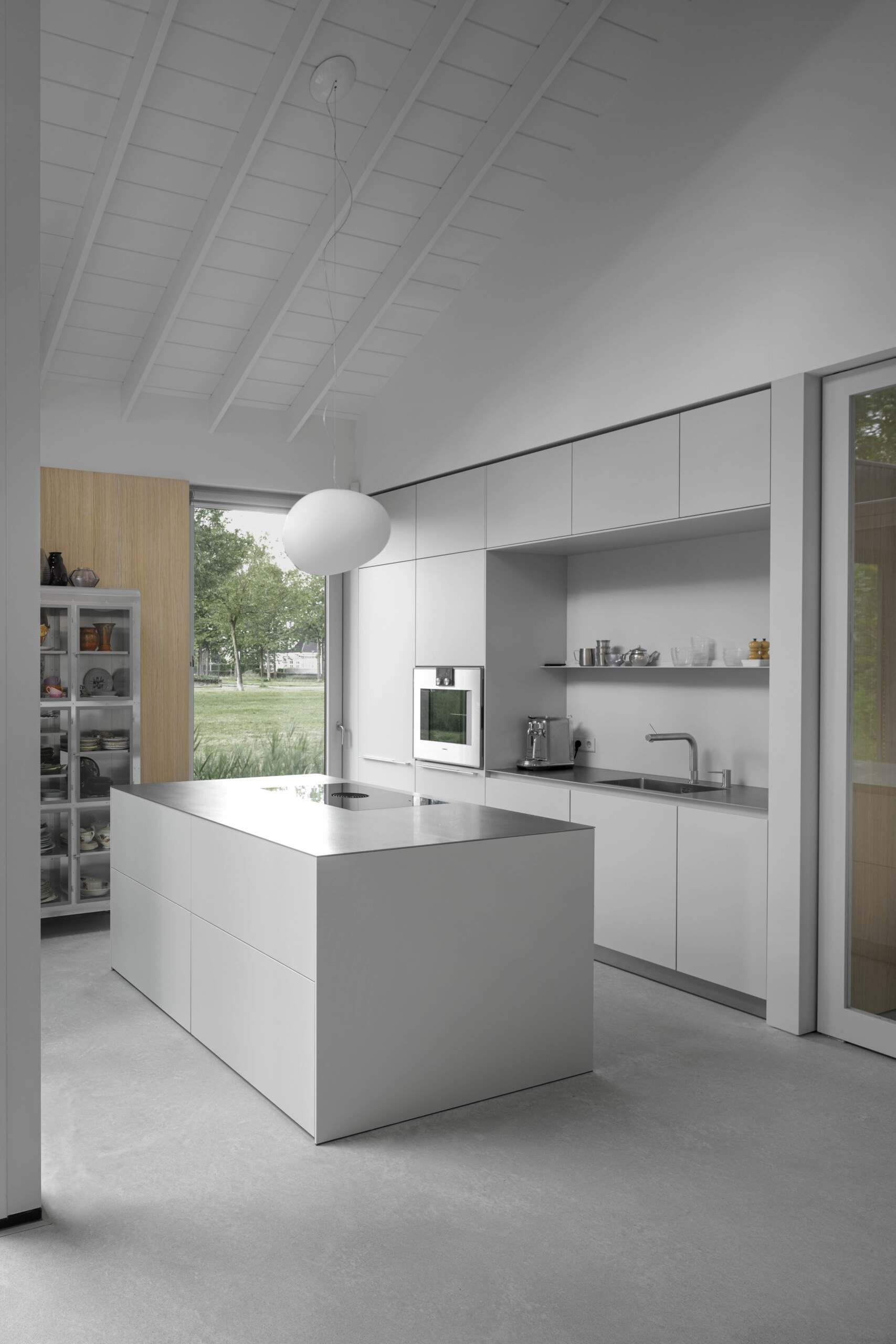 This kitchen includes minimalist hardware-free cabinetry that complements the surrounding wall panels, with horizontal lines that draw the eye and enhance the feeling of space. Its placement alongside the patio offers a unique indoor-outdoor flow, allowing the kitchen to extend into the garden during warmer months.