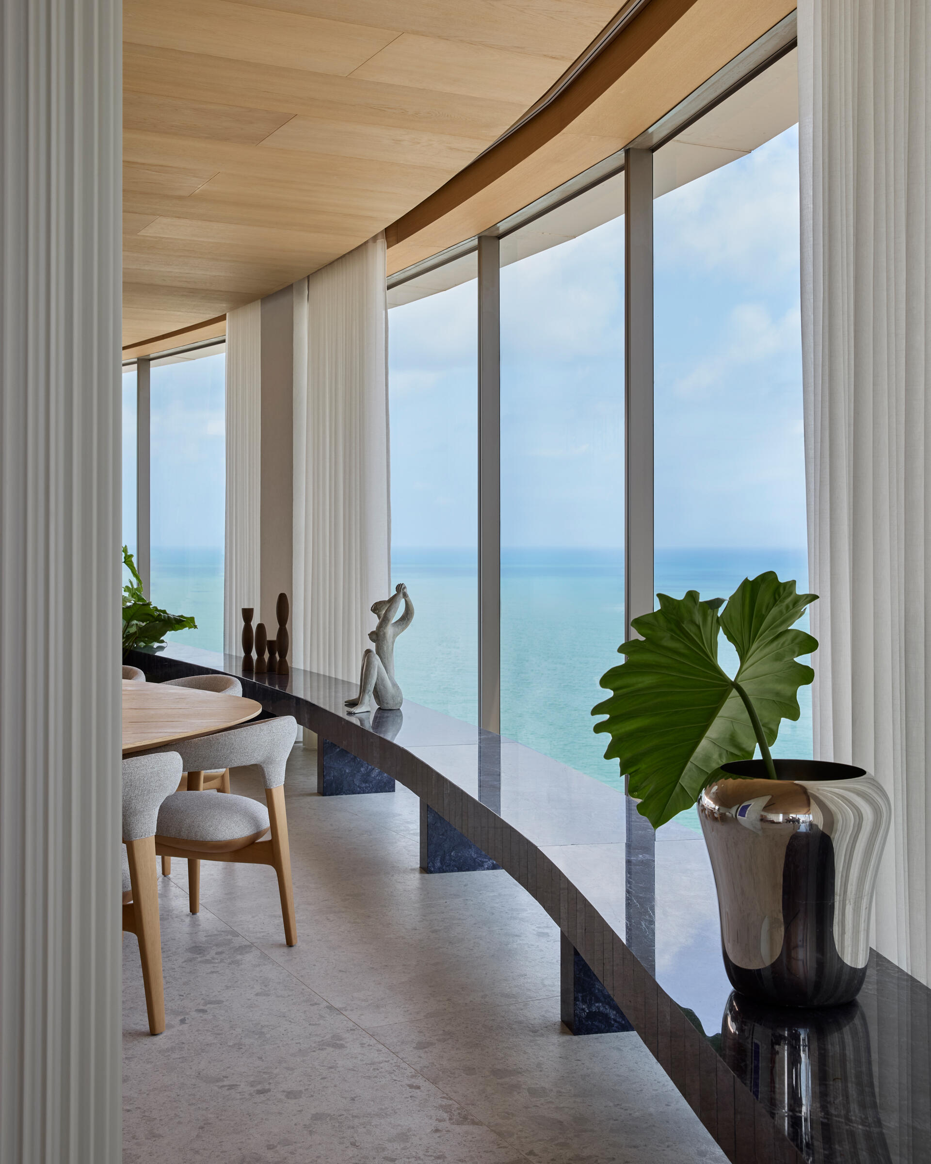 A full wall of windows frames panoramic ocean views in this Recife apartment. Neutral tones and curved furniture keep the focus on the horizon.