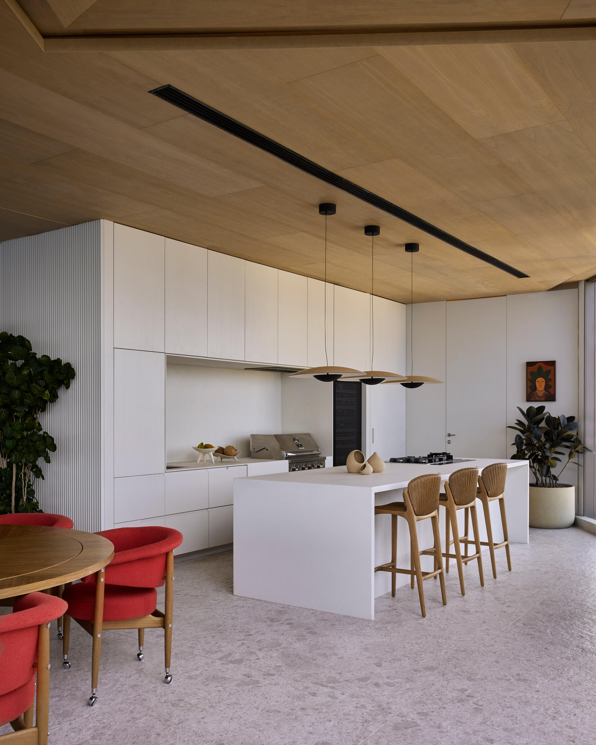 The kitchen and barbecue area share the upper floor with the main social spaces. The kitchen features a countertop clad natural stone, while the blue cabinetry echoes the tones of the sea. Materials and layout of the barbecue area emphasize openness and continuity, with finishes chosen to unify the communal areas.