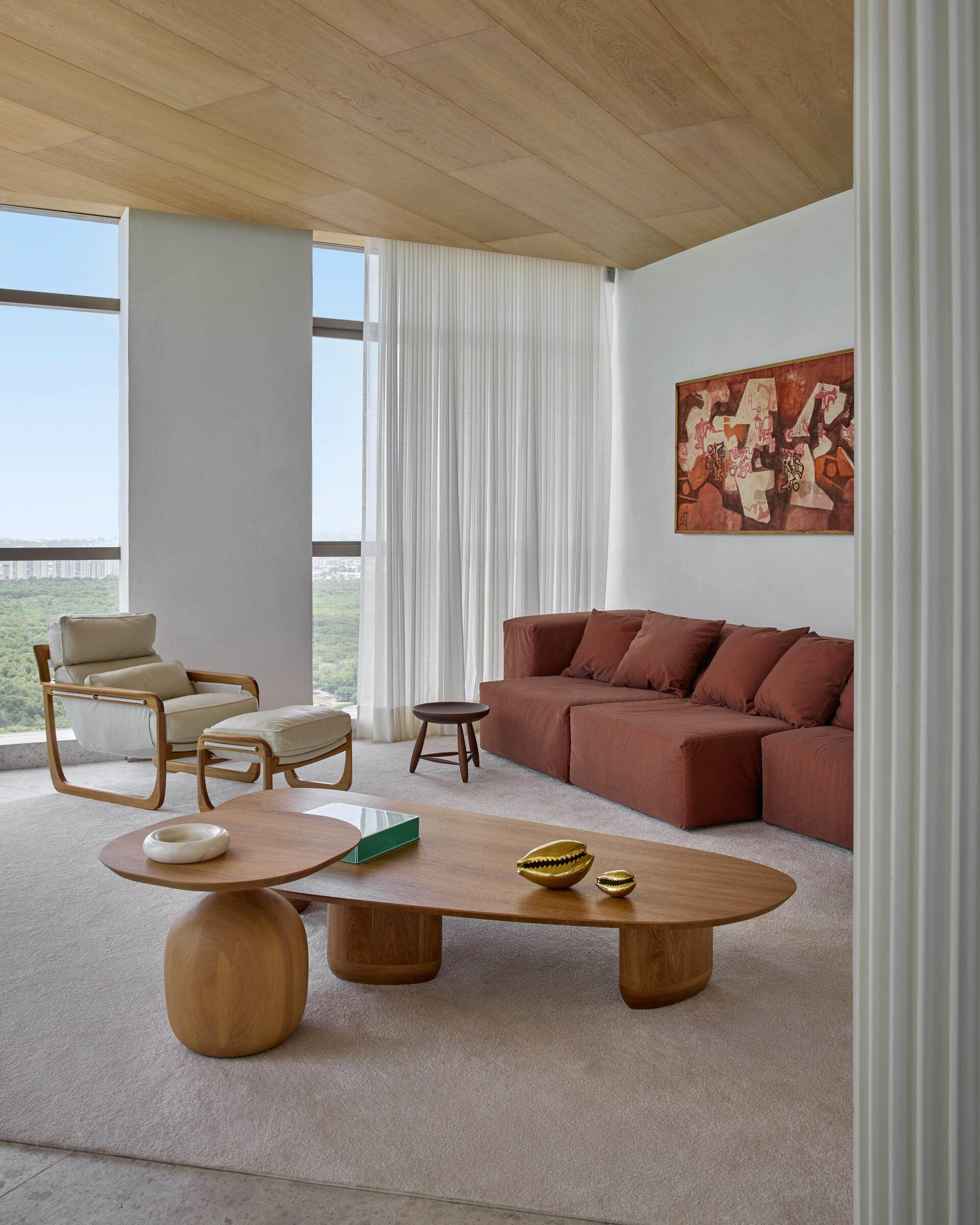 A second living space introduces a striking contrast through a rusty-colored couch. Surrounded by a more restrained palette, the color becomes a visual anchor within a calm environment. This space offers an alternative setting for quiet retreat or informal gatherings, without disrupting the overall tone of the apartment.