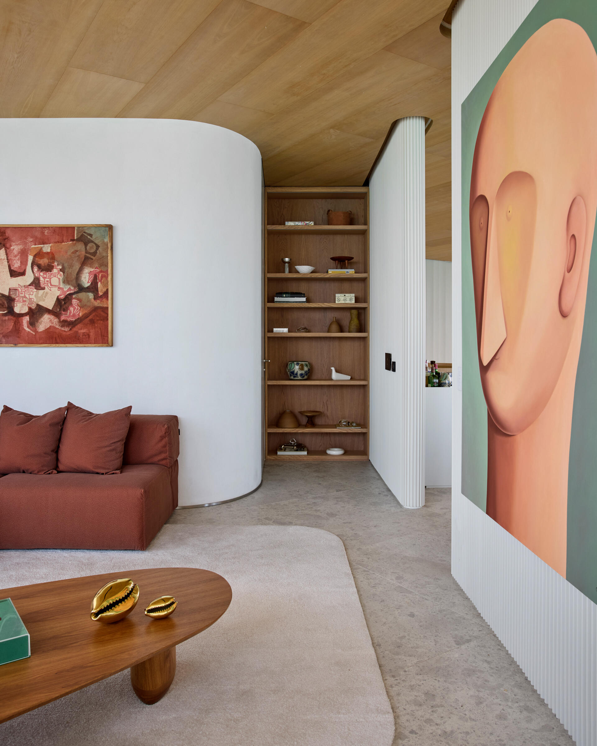 A second living space introduces a striking contrast through a rusty-colored couch. Surrounded by a more restrained palette, the color becomes a visual anchor within a calm environment. This space offers an alternative setting for quiet retreat or informal gatherings, without disrupting the overall tone of the apartment.