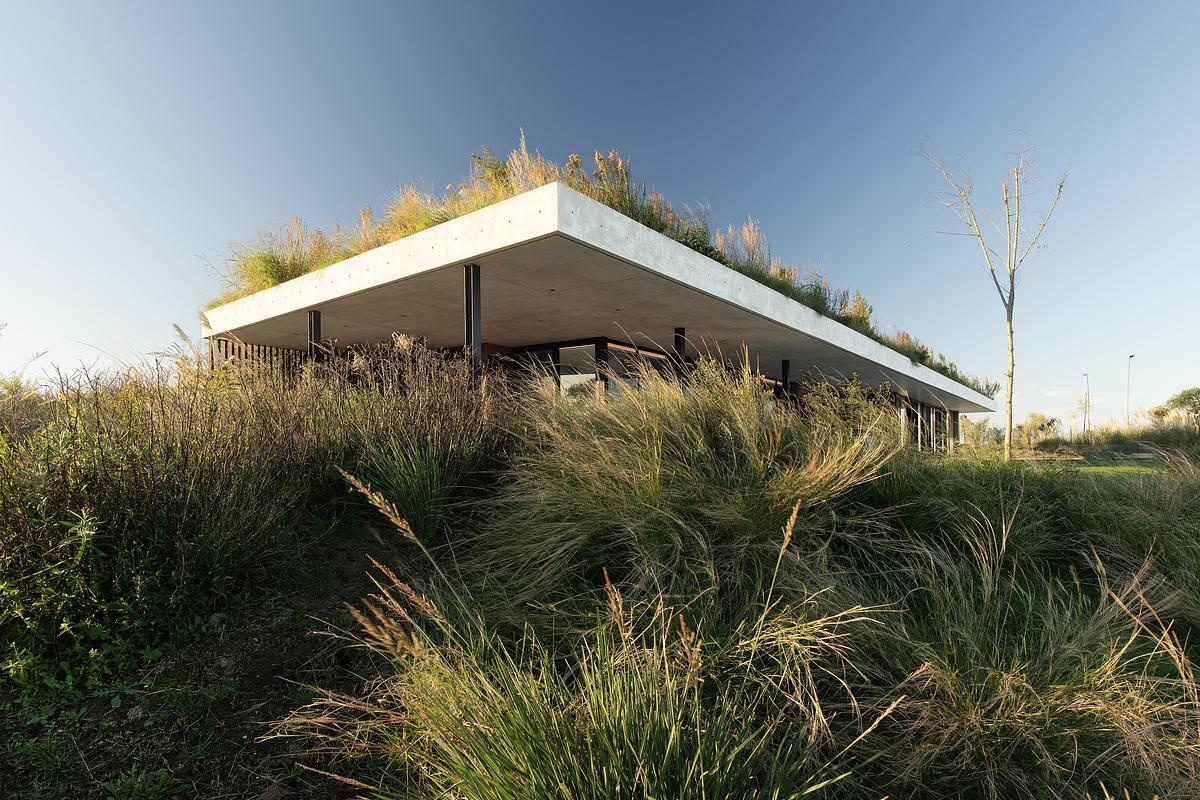 This concrete shell of this modern club house does double duty: it acts as both the building’s structure and surface, minimizing visual clutter and material use. The result is a continuous architectural form that feels quiet yet confident, merging seamlessly with its environment while inviting people to explore, gather, and linger.