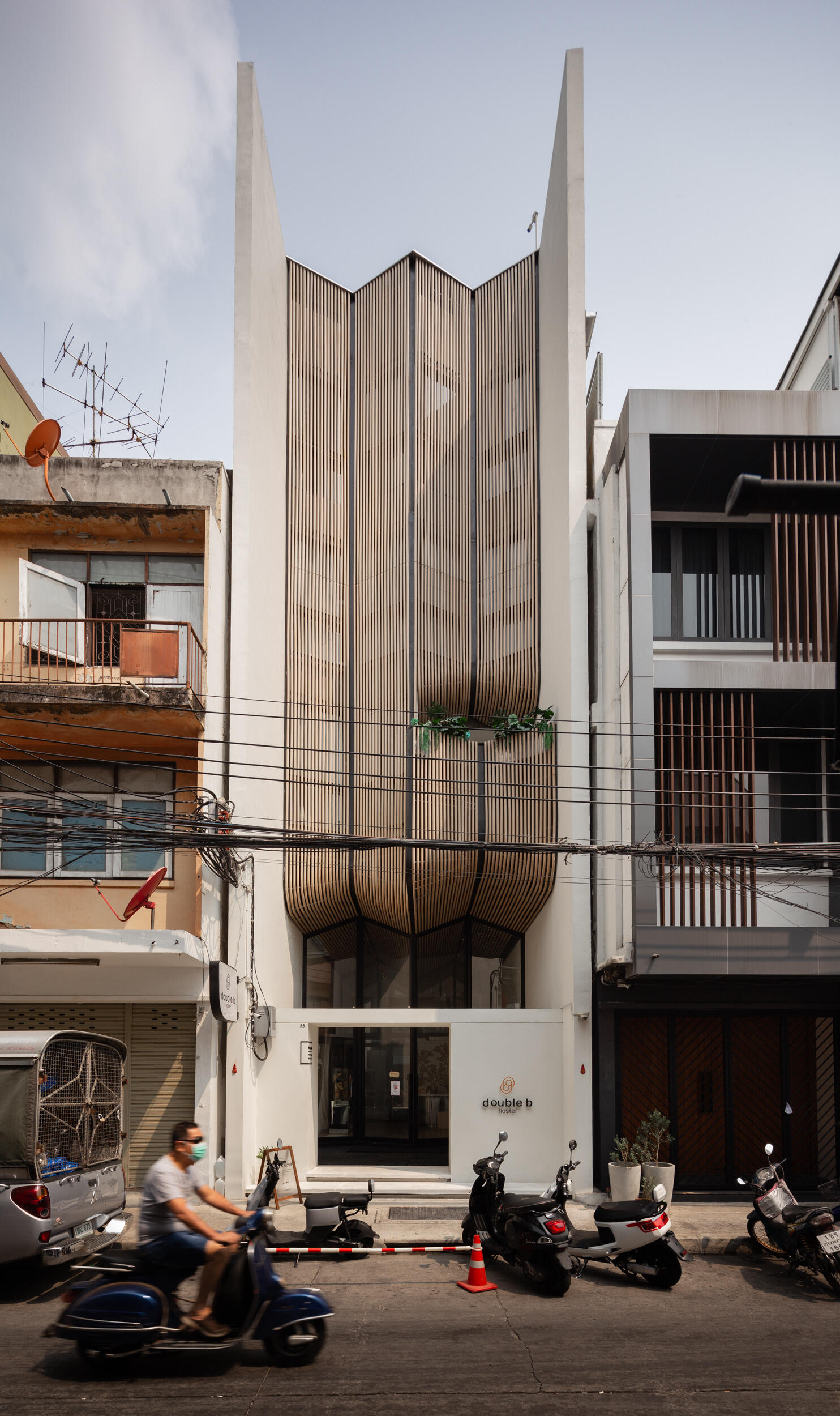 The Double B Hostel’s exterior facade features flowing wooden waves crafted from composite rods, blending traditional craftsmanship with modern design to stand out in Bangkok’s dense old town.