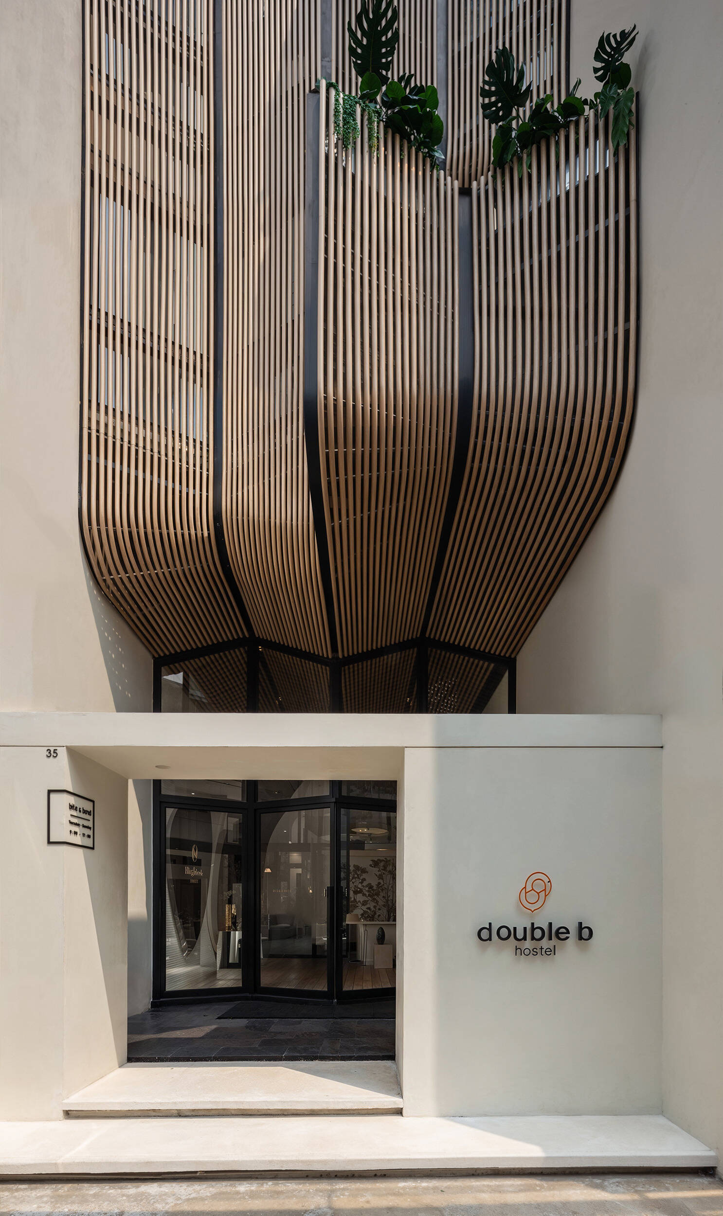 The Double B Hostel’s exterior facade features flowing wooden waves crafted from composite rods, blending traditional craftsmanship with modern design to stand out in Bangkok’s dense old town.