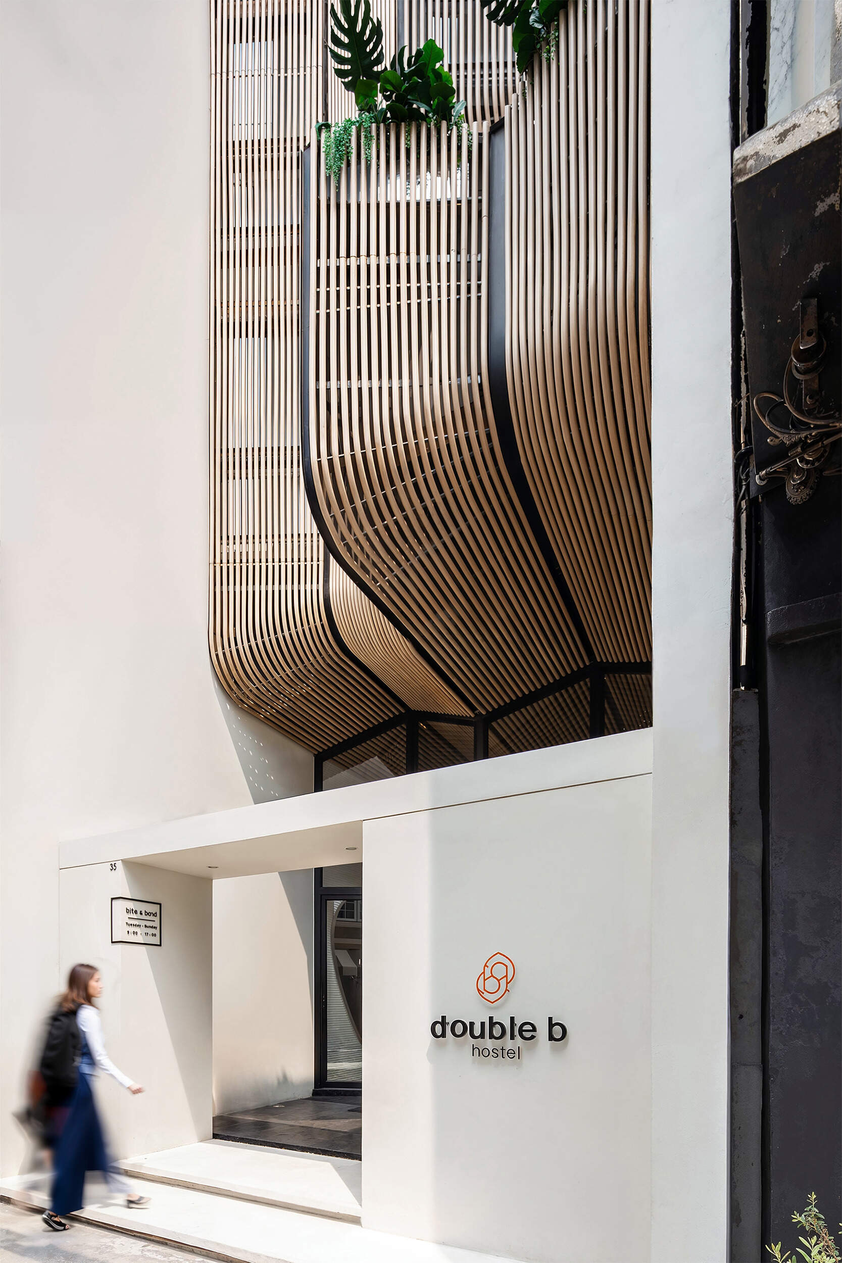 The Double B Hostel’s exterior facade features flowing wooden waves crafted from composite rods, blending traditional craftsmanship with modern design to stand out in Bangkok’s dense old town.